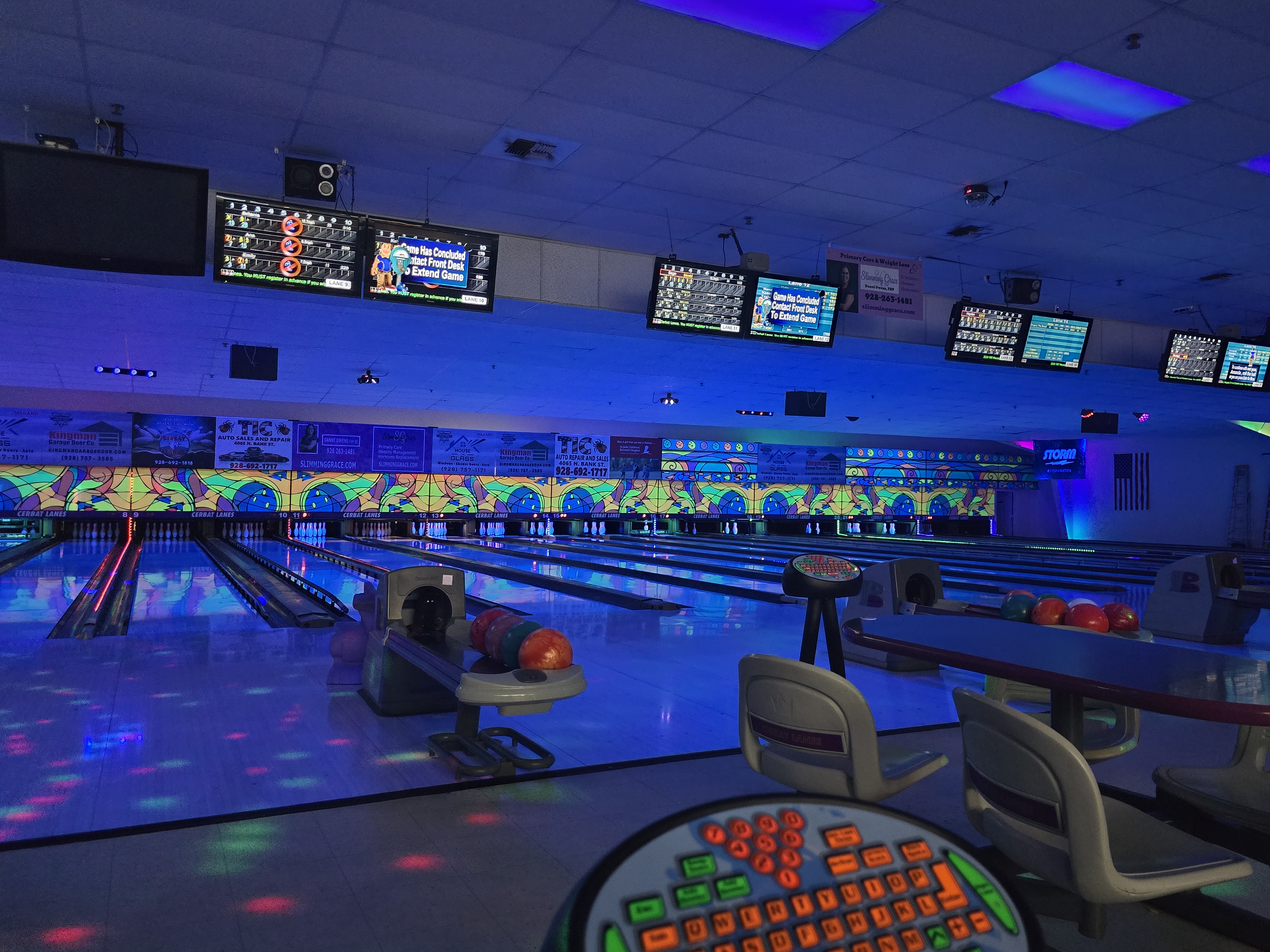 Bowling lanes illuminated with blue and purple cosmic lighting, showing bowling balls and scoring monitors.