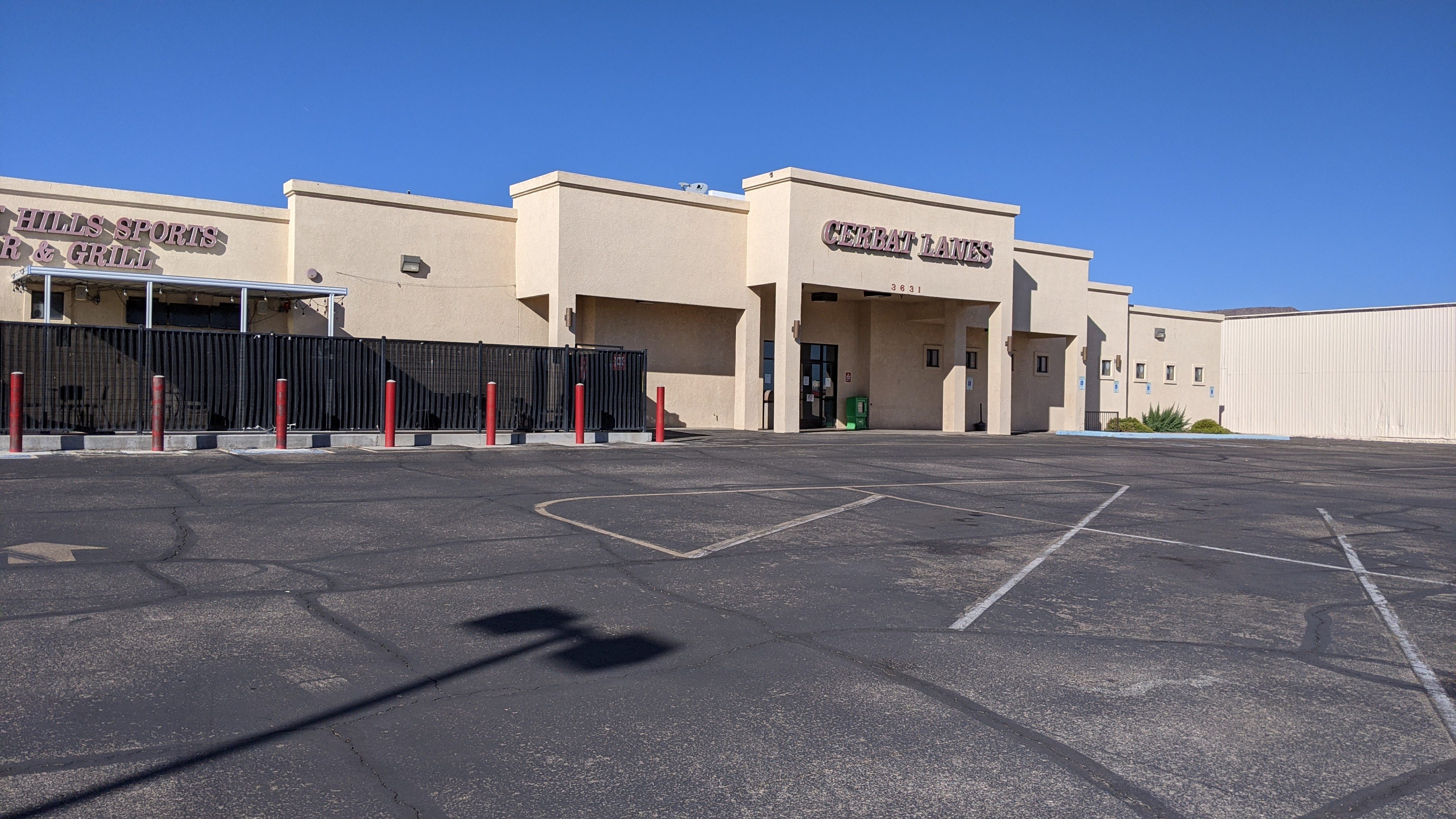Exterior view of Cerbat Lanes with its large parking lot and adjacent Hills Sports Bar & Grill under a clear blue sky.