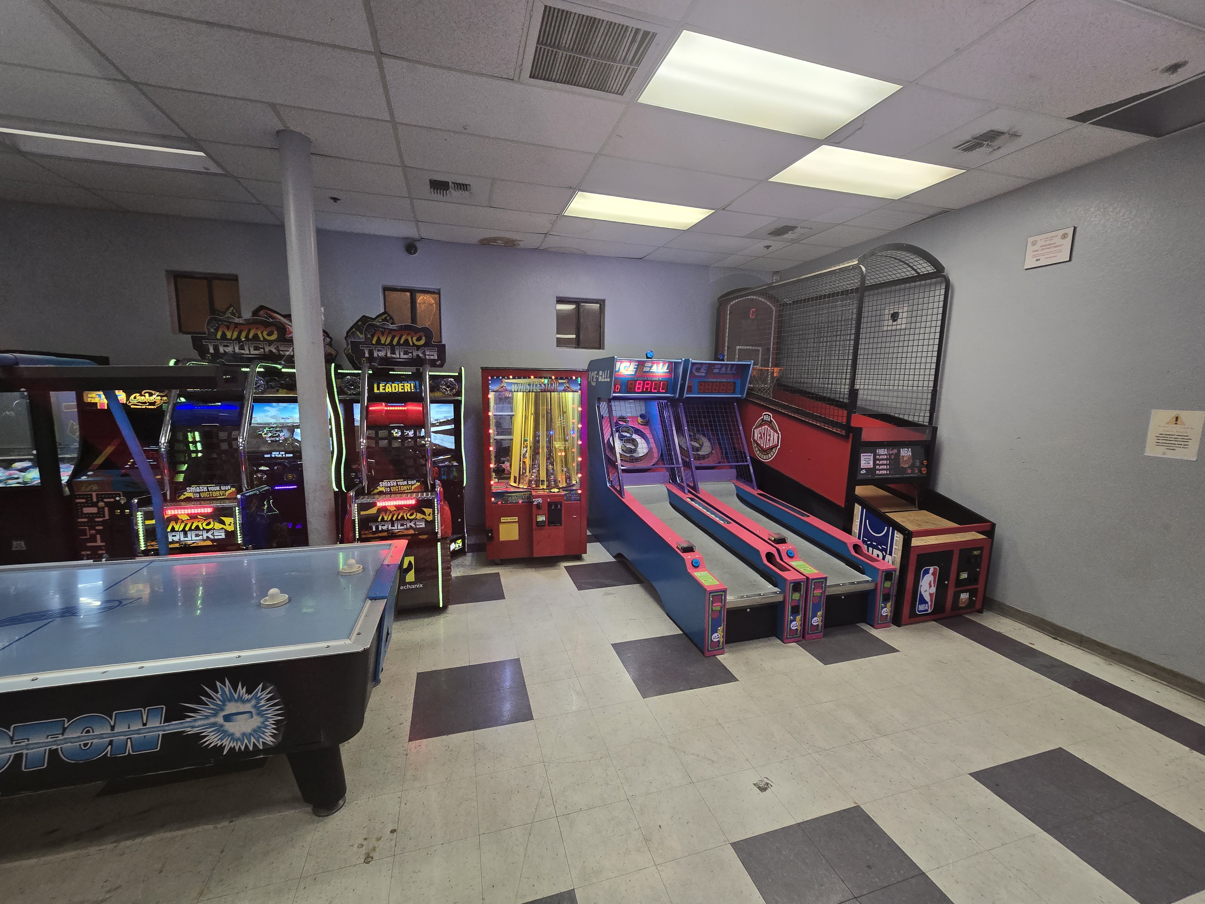 An indoor arcade room with several games, including air hockey, driving games, skeeball, and a prize machine.