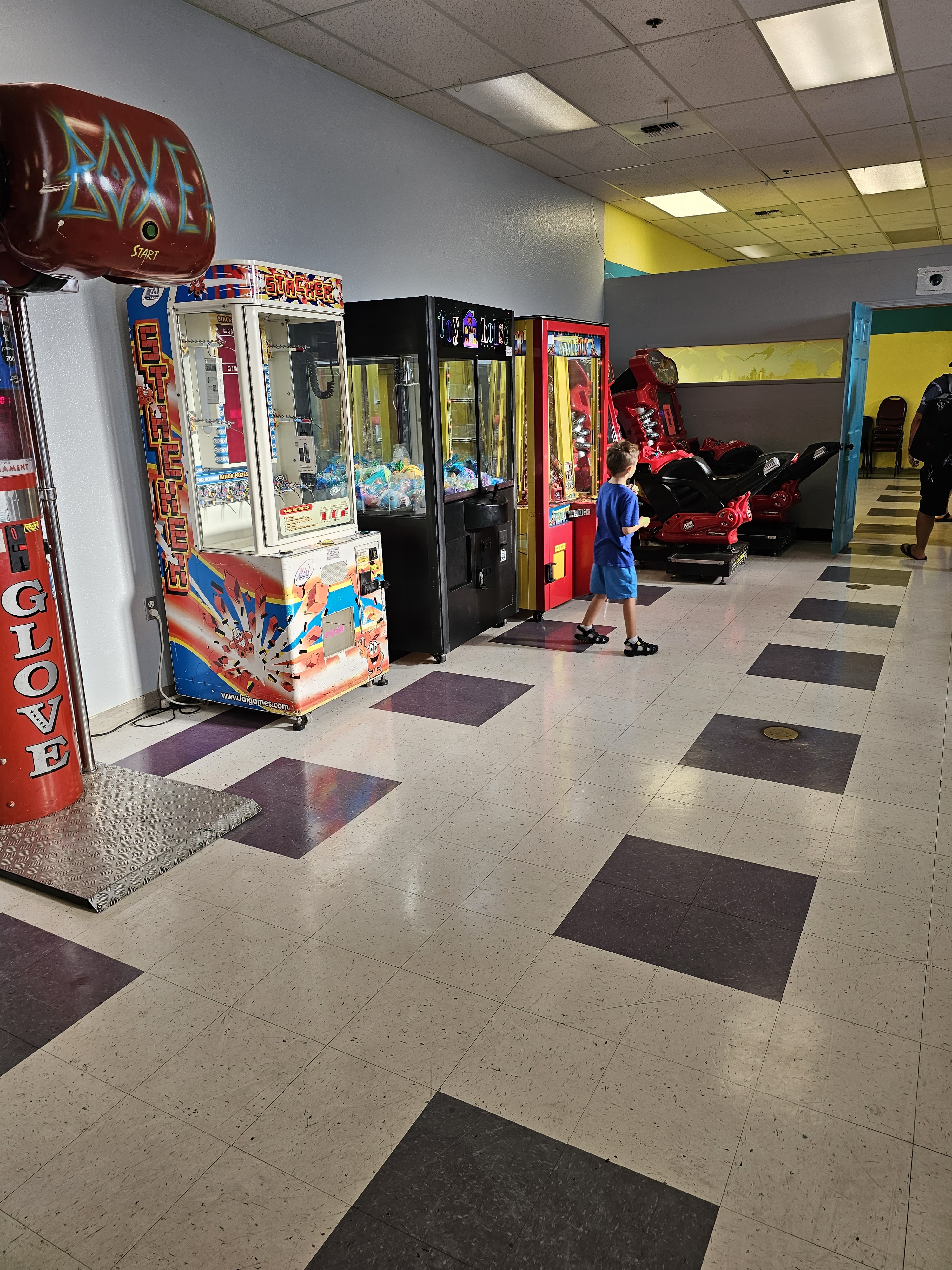 A young boy walks past a row of colorful arcade games including claw machines and a boxing game.