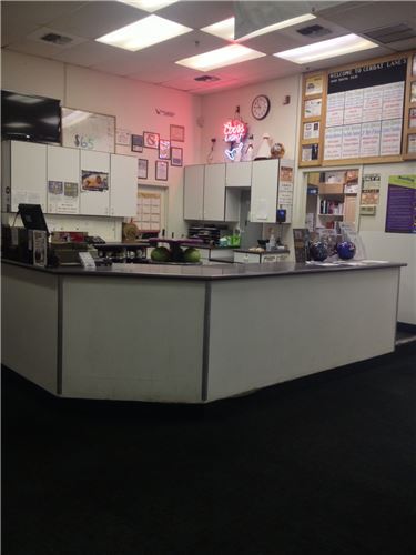 A brightly lit front desk area with a neon 'Coors Light' sign and a large information board on the wall.