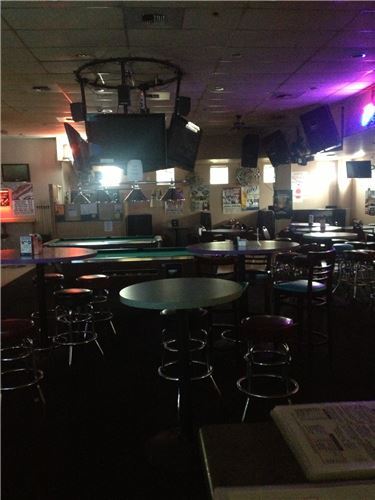 A dimly lit bar and lounge area with high-top tables, stools, multiple televisions, and a billiards table.
