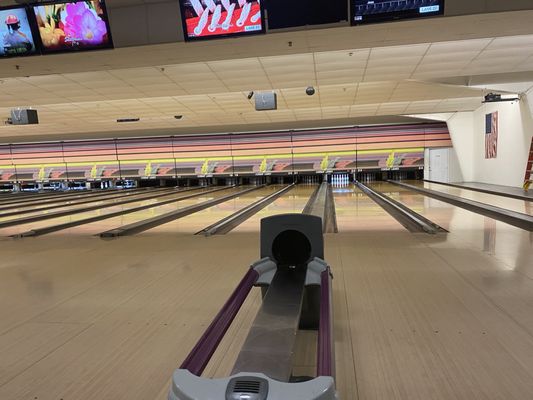 A view of several polished bowling lanes with overhead monitors and a ball return at Cerbat Lanes.