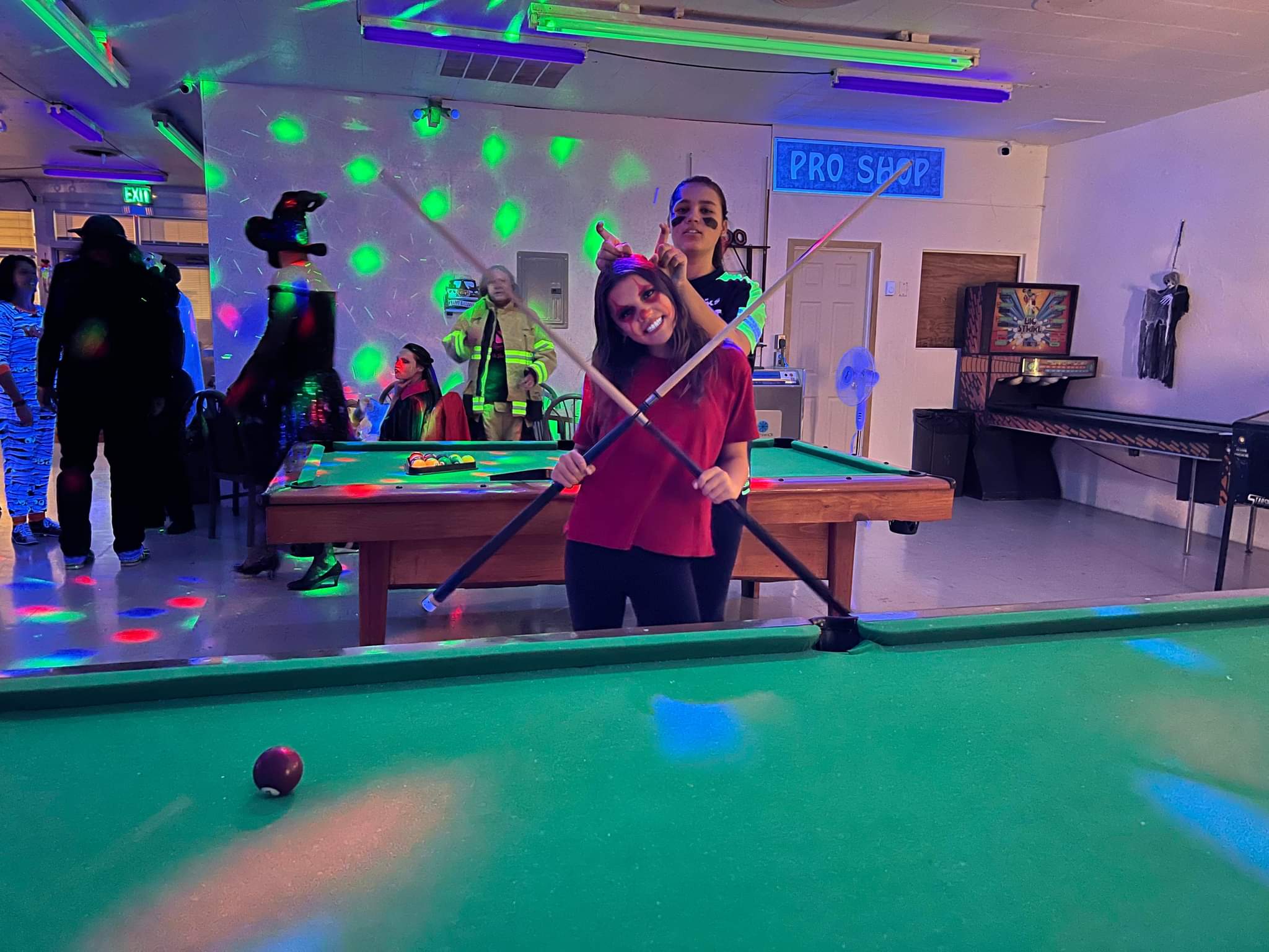 People in Halloween costumes pose with pool cues in a neon-lit billiard room at a bowling center.