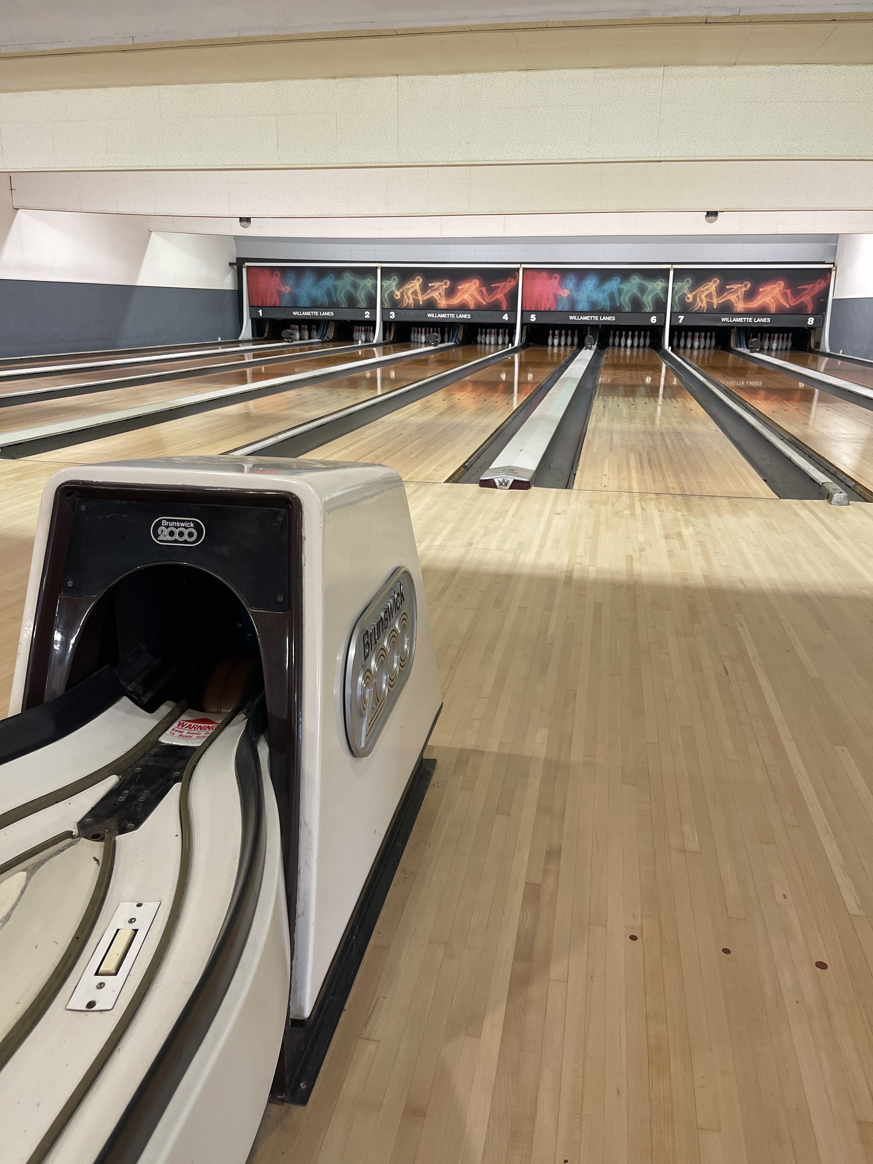 Eight polished bowling lanes with colorful bowler graphics and a vintage Brunswick 2000 ball return in the foreground.