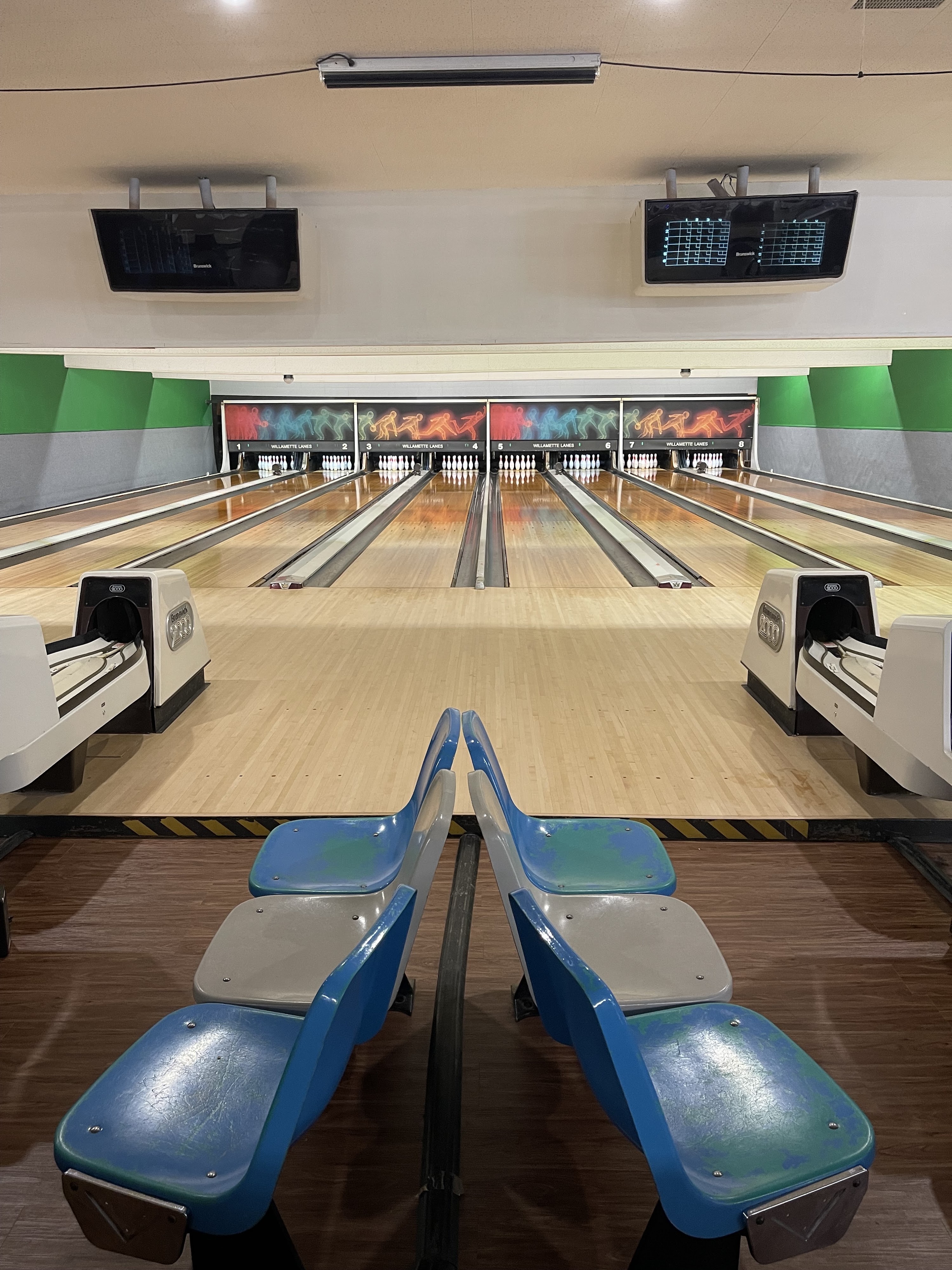 A symmetrical view of eight polished bowling lanes with blue and grey seating in the foreground.