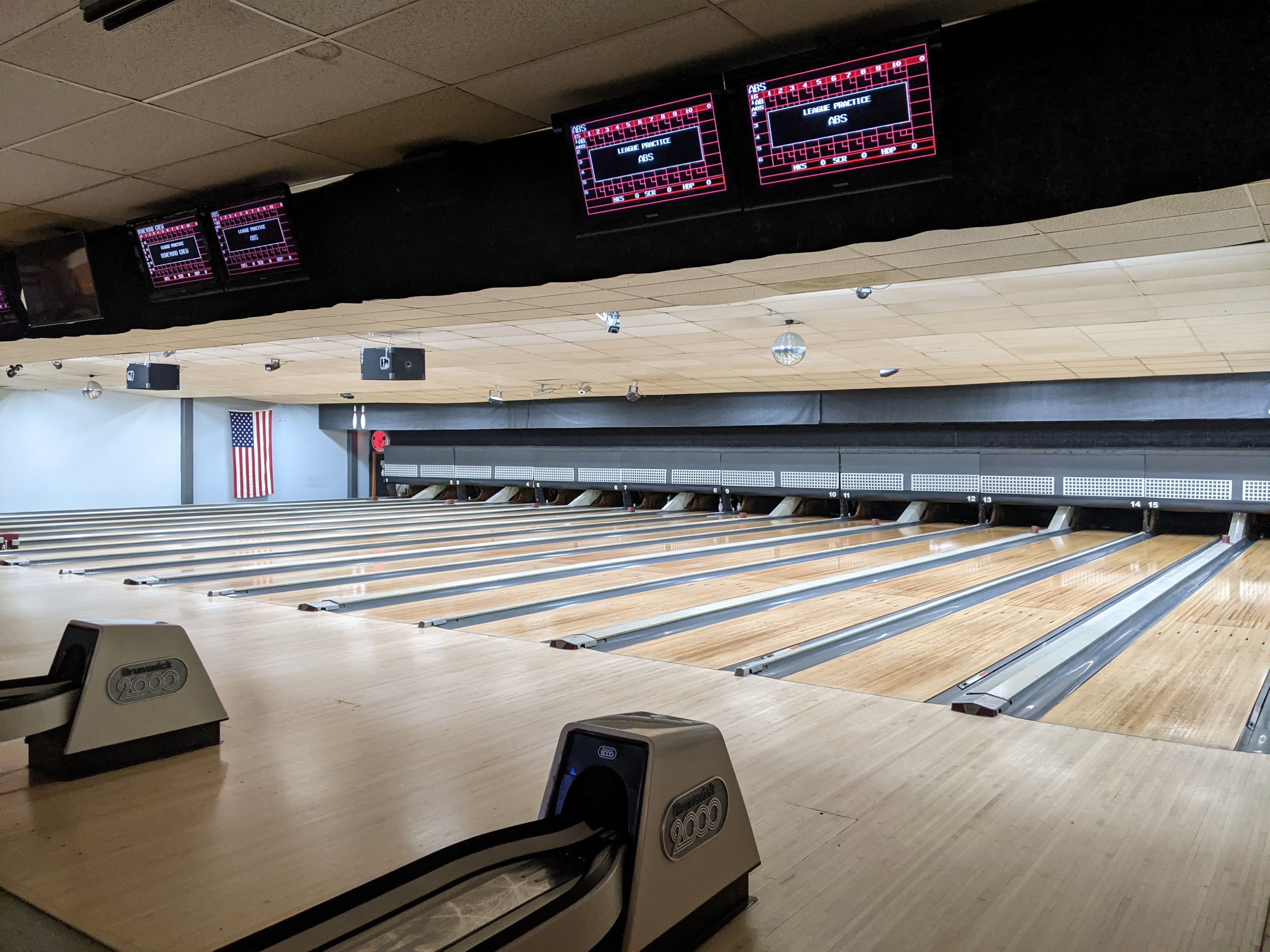 Wide view of polished wood bowling lanes with overhead scoring monitors and ball returns at Milwaukie Bowl.