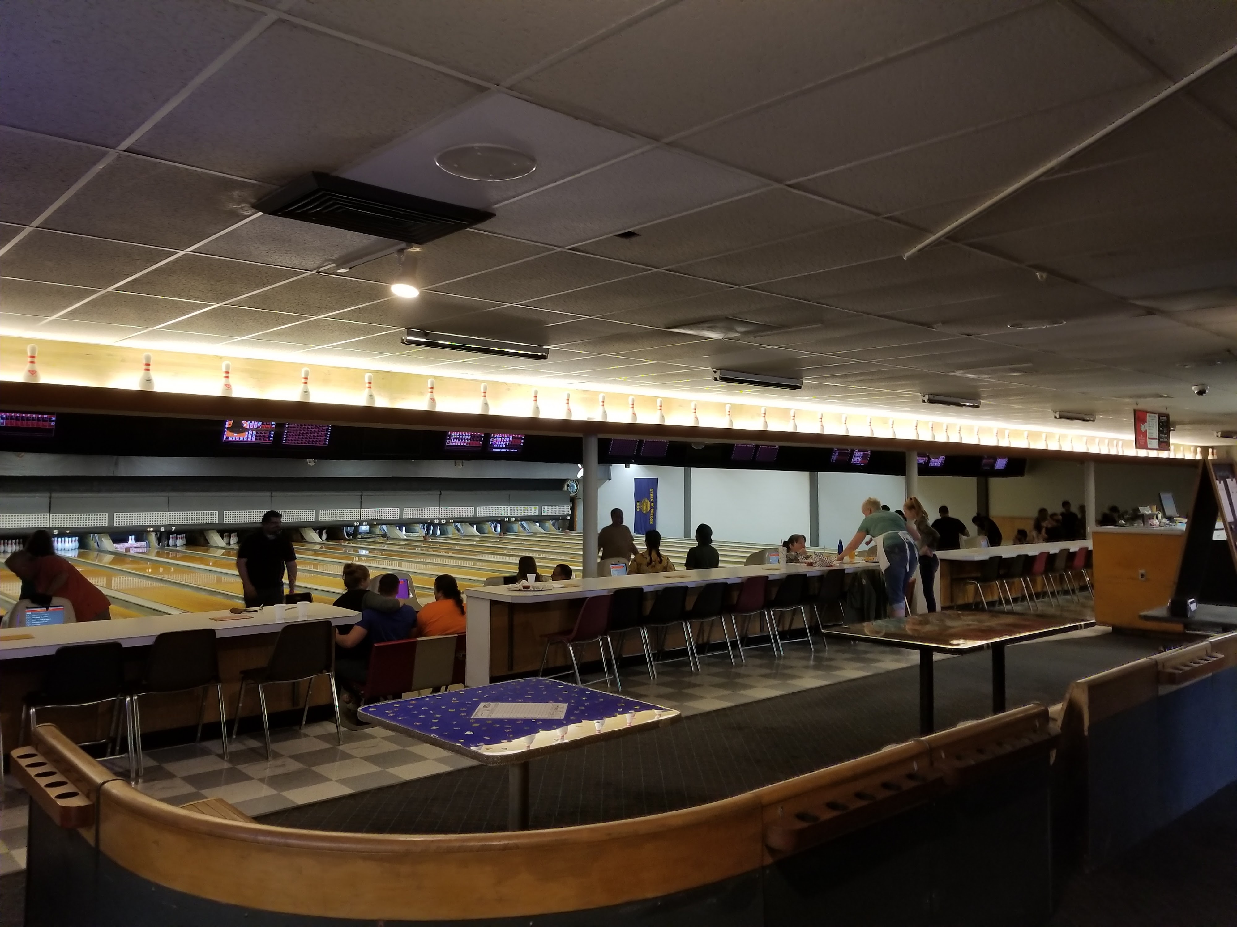 People sitting and bowling at a center with several lanes and overhead scoring monitors.