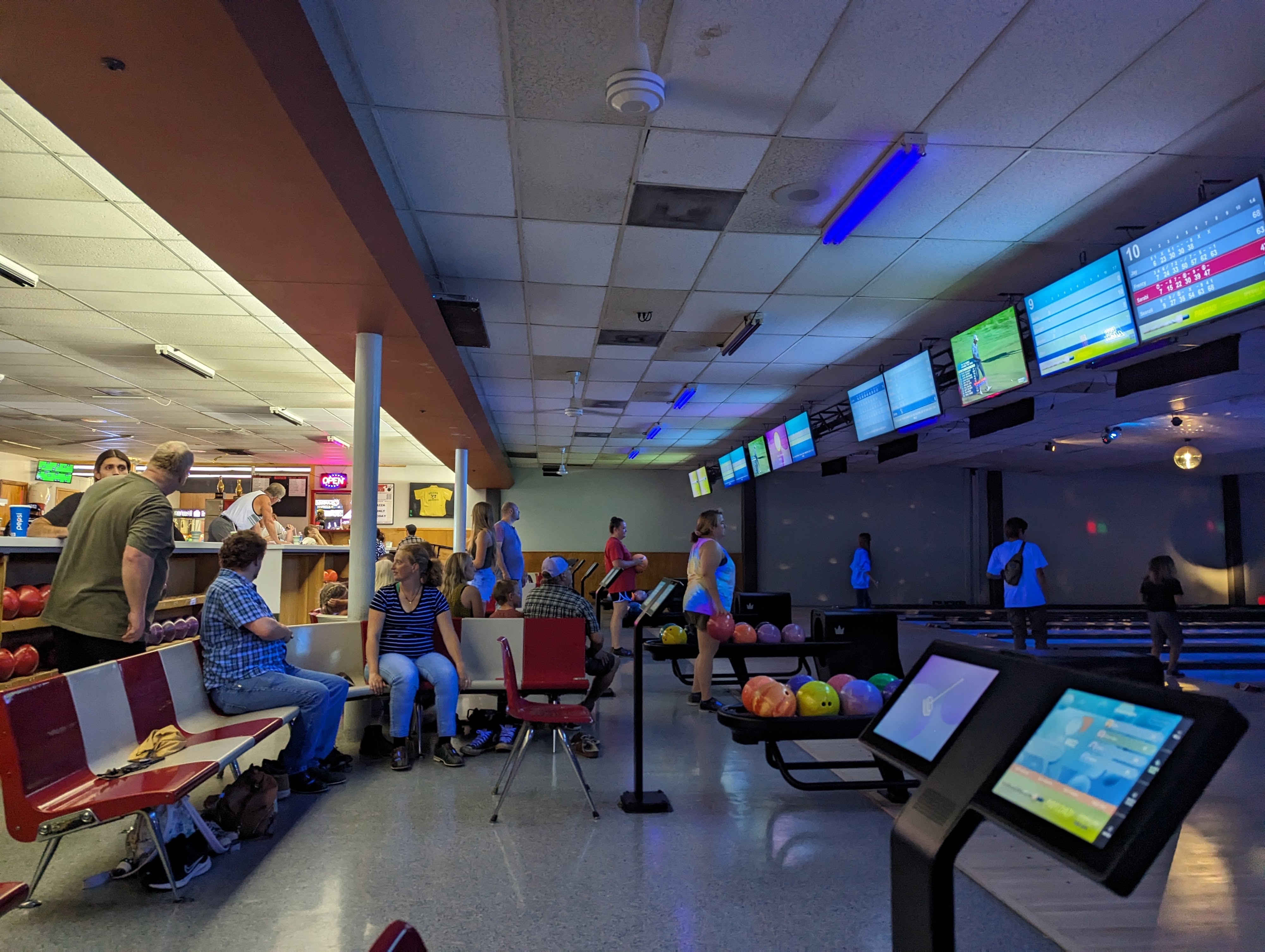 A lively bowling alley interior with groups of people, retro seating, and modern digital scoring monitors.