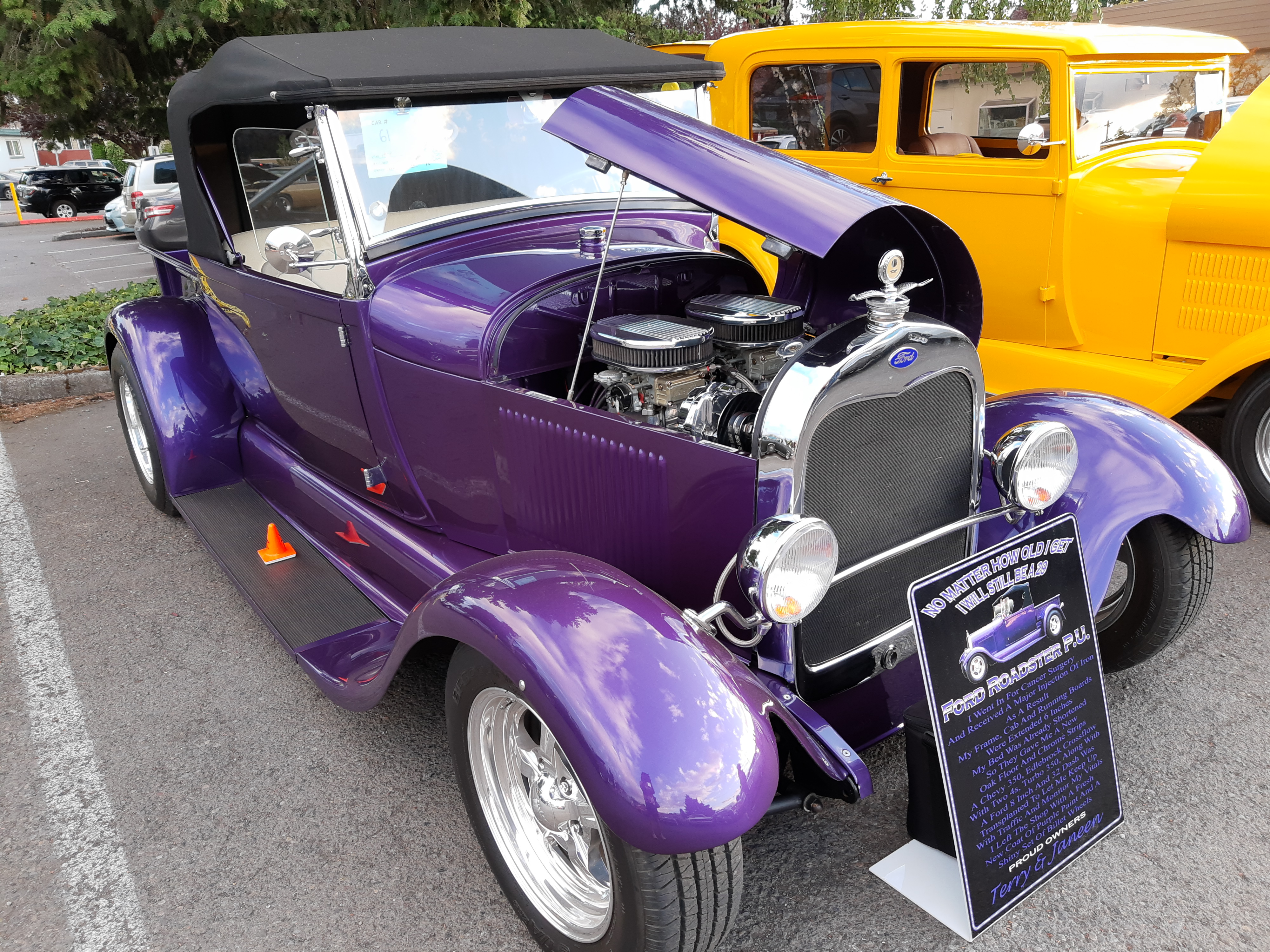A vintage purple Ford Roadster with an open hood showing a chrome engine at a parking lot car show.
