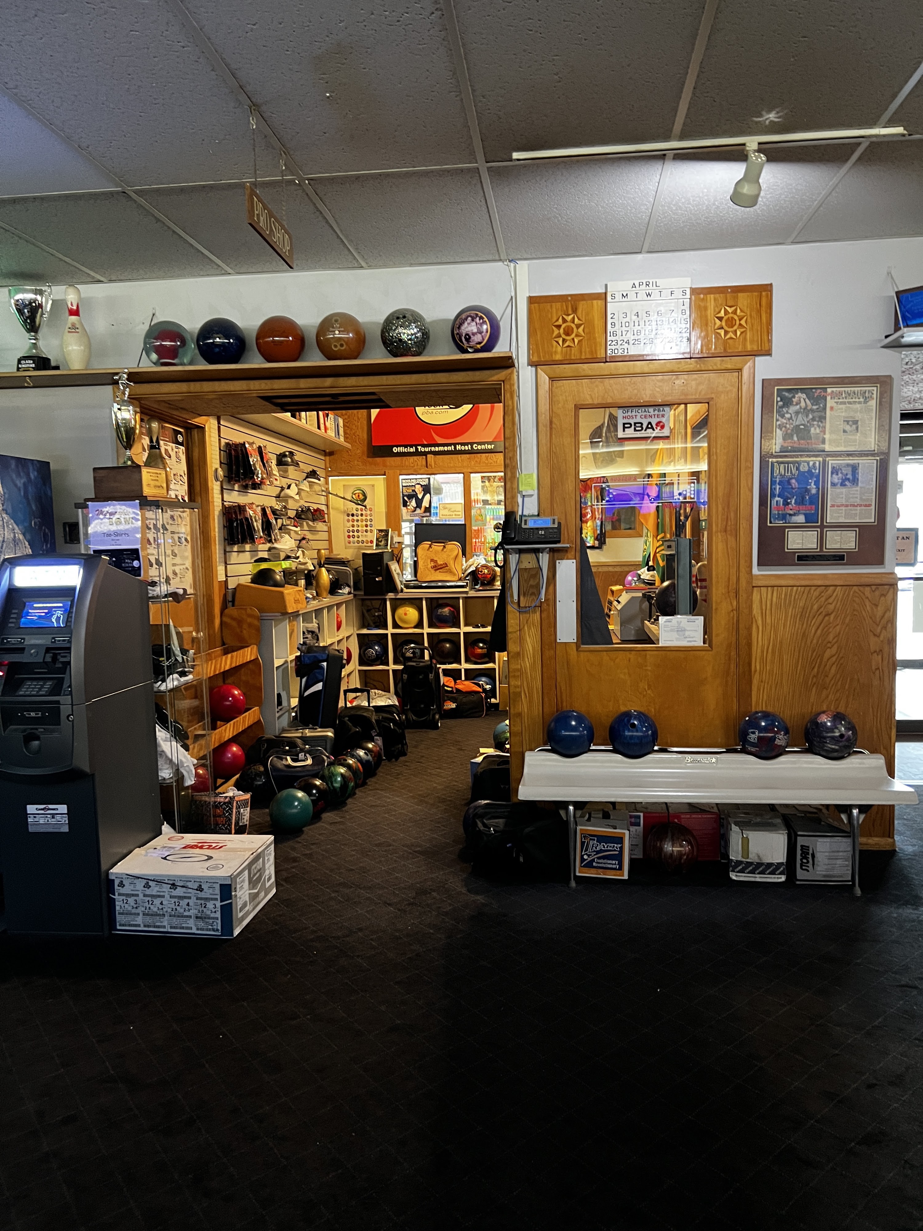 An indoor view of a bowling center pro shop entrance filled with bowling balls, bags, and trophies.