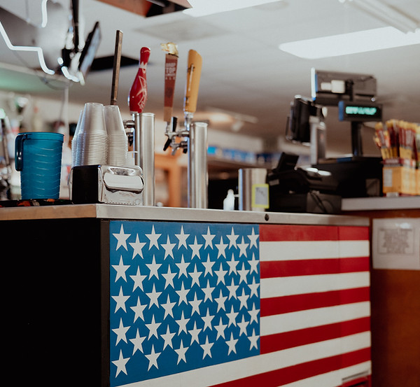 A snack bar counter with an American flag design featuring beer taps and stacks of cups.
