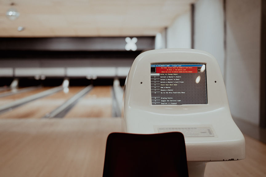 Close-up of a vintage automatic scoring console with bowling lanes blurred in the background.