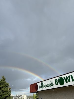 A double rainbow spans across a dark, cloudy sky over the Milwaukie Bowl exterior sign.