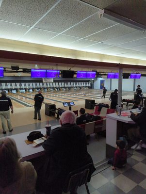 Bowling lanes at Milwaukie Bowl with people playing and purple scoring monitors overhead.