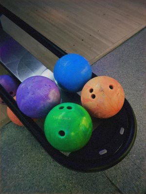 Close-up of green, purple, blue, and orange house bowling balls on a black ball return rack.