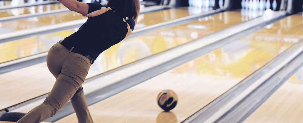 A person in mid-follow-through after releasing a bowling ball down a polished wooden lane toward the pins.