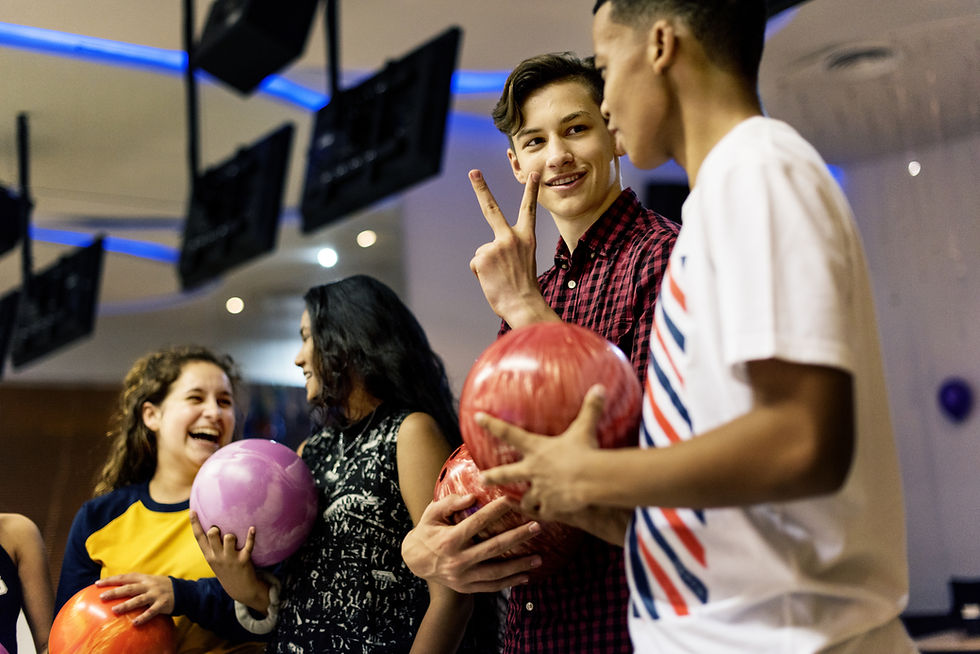 Four smiling young adults holding bowling balls and laughing together at a bowling alley.