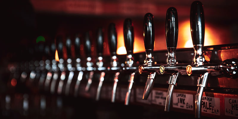 A long row of chrome beer taps with black handles under warm bar lighting.