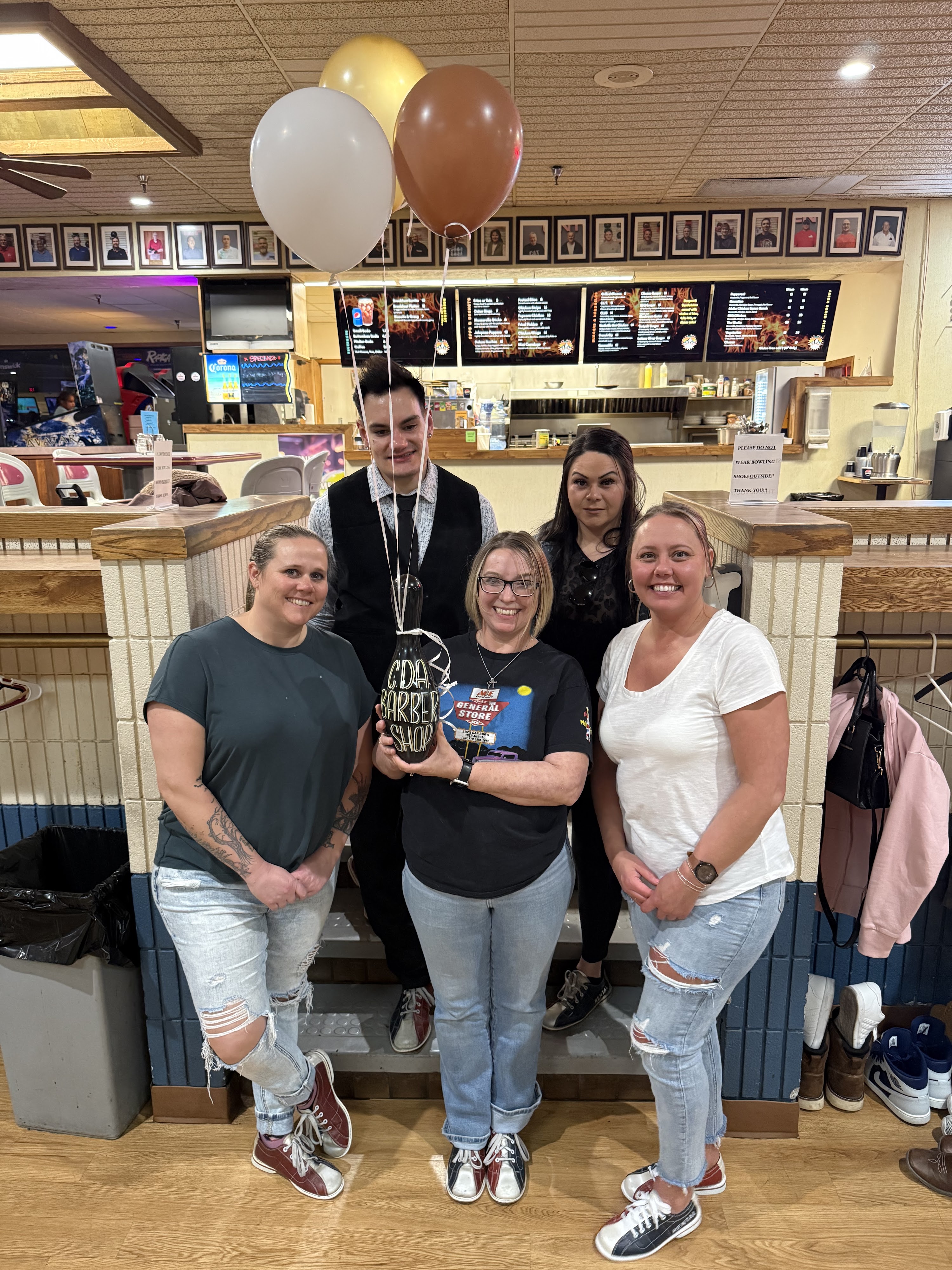 Five people holding a custom barber shop bowling pin trophy in front of a snack bar menu at a bowling center.