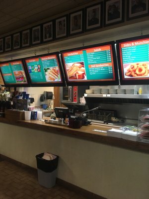 A bowling alley snack bar counter with four digital menu boards showing food and drink options.