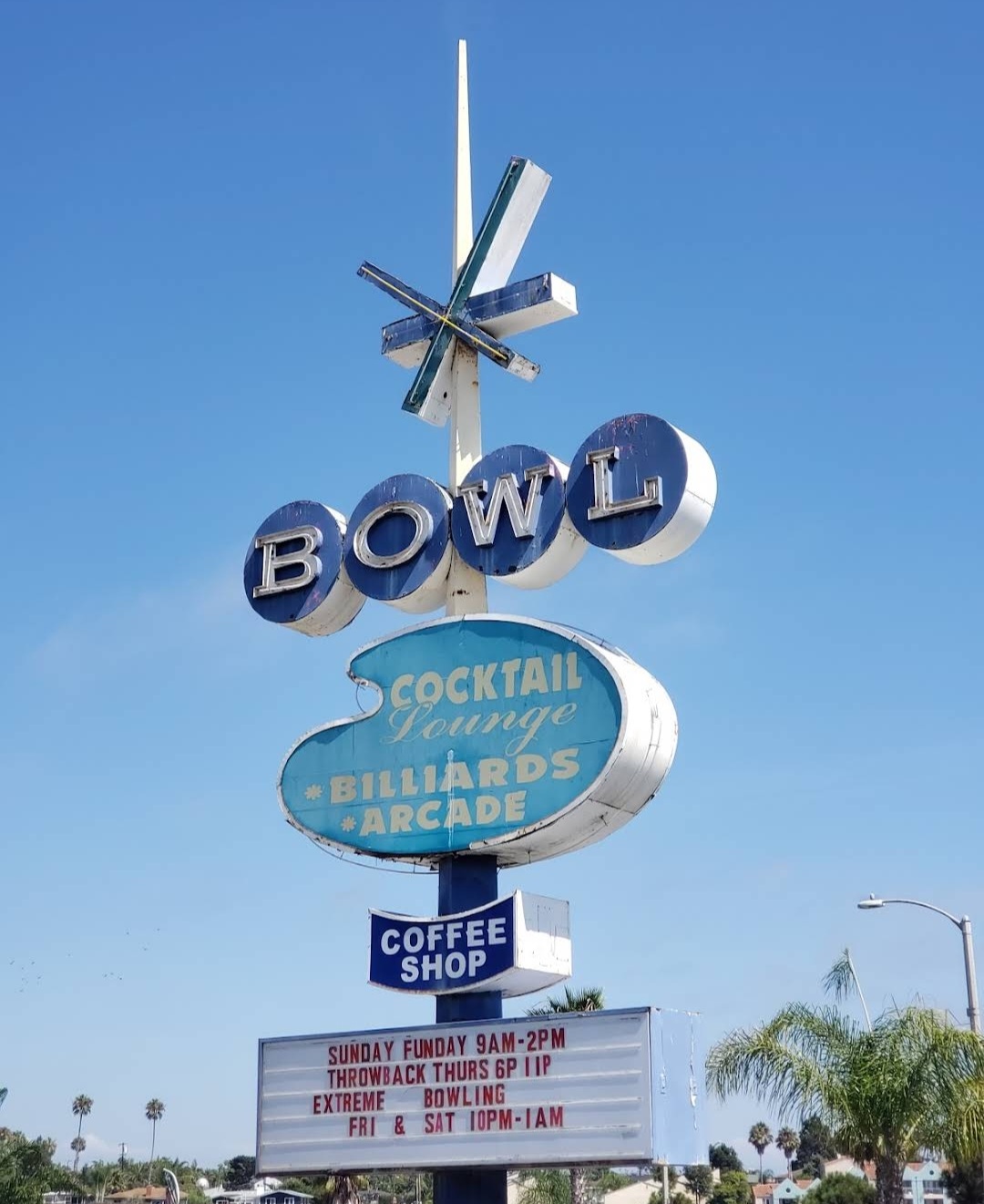 A tall vintage neon sign for Surf Bowl against a clear blue sky, advertising billiards, arcade, and extreme bowling.