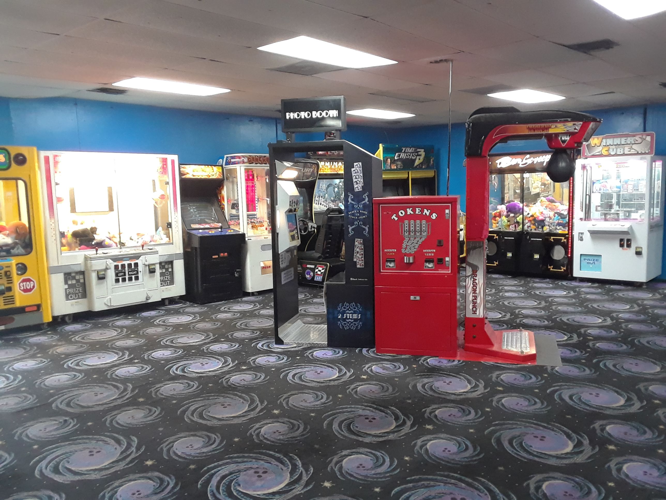 An arcade area with various claw machines, a photo booth, and a punching game on a cosmic-themed carpet.
