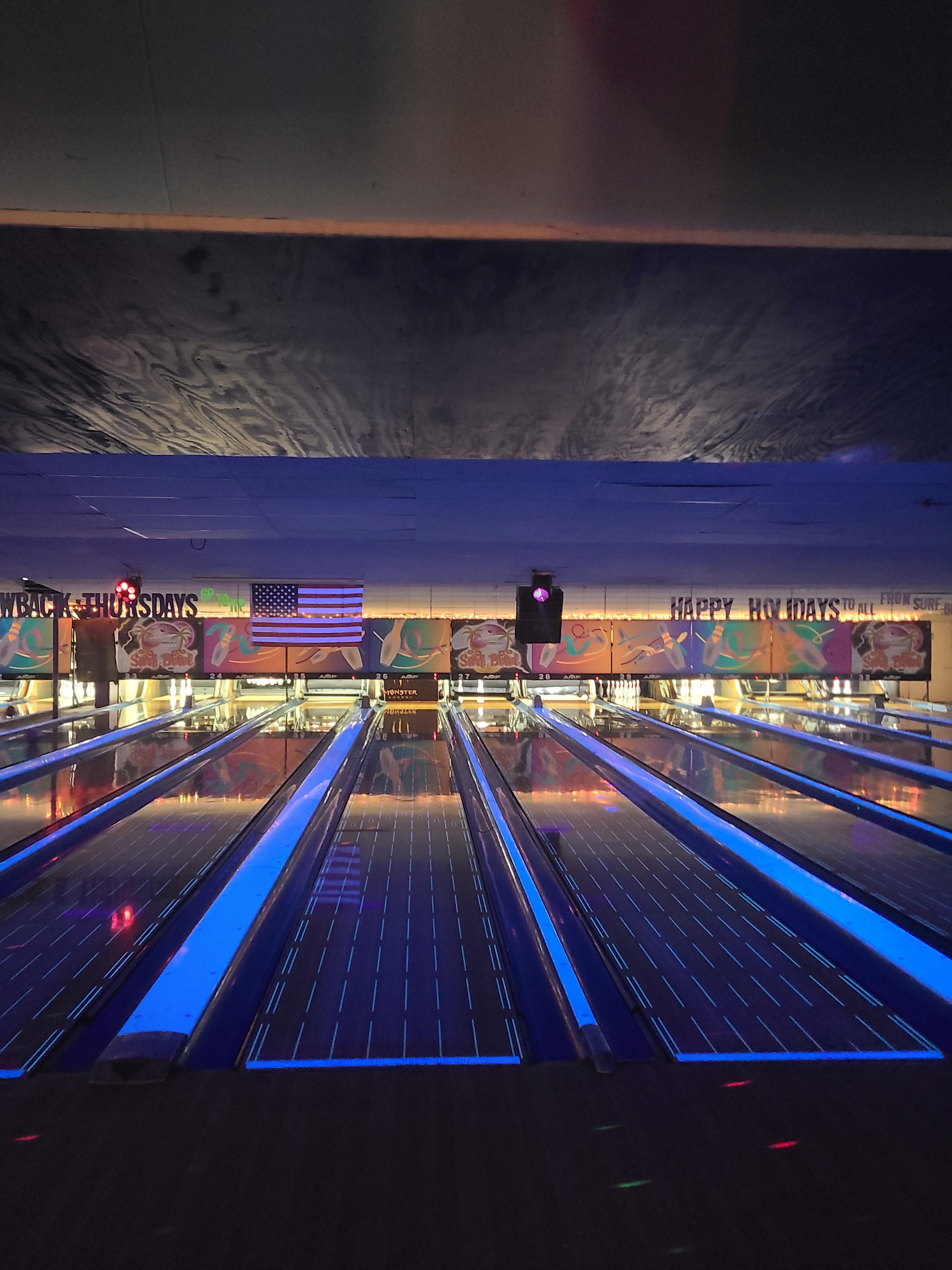A series of bowling lanes illuminated with bright blue neon lights under cosmic conditions.