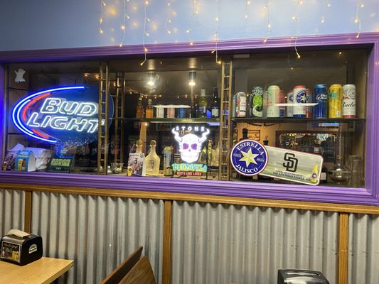 A bar display with neon beer signs, a San Diego Padres logo, and string lights inside a purple frame.