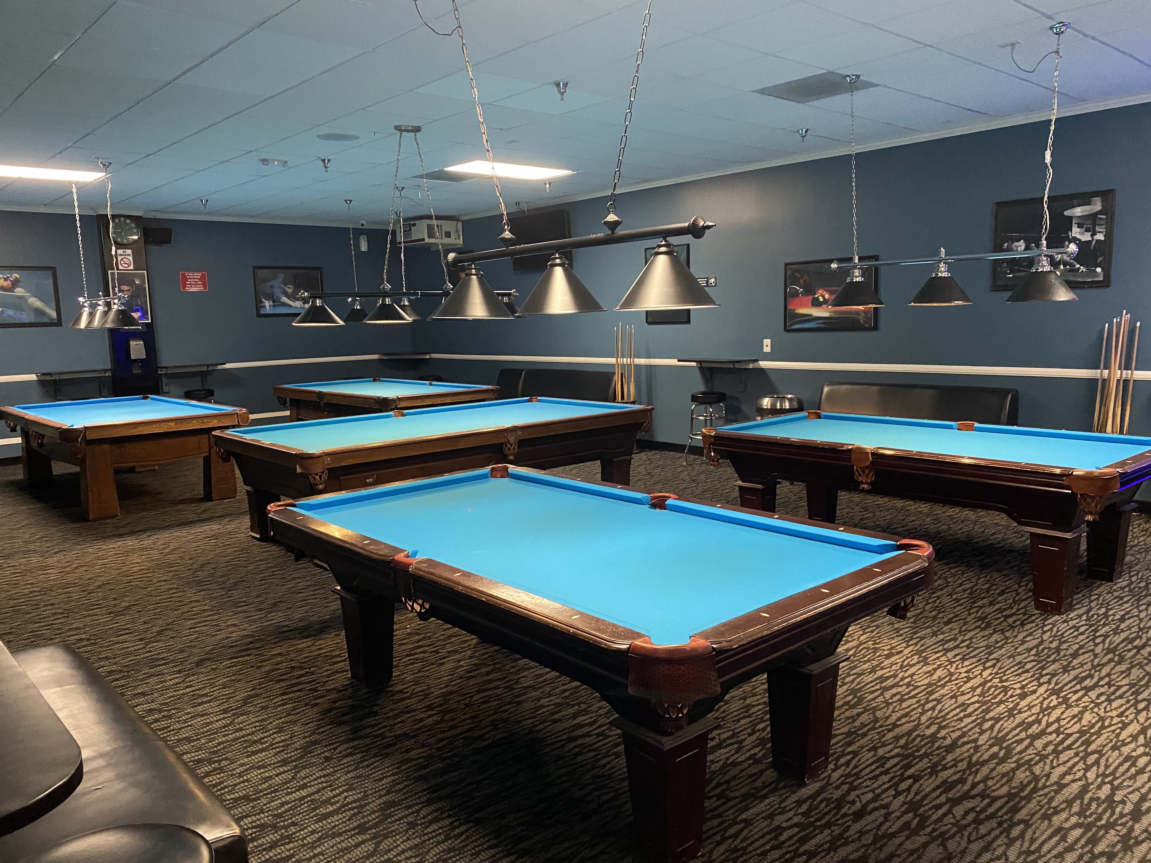 A room filled with five professional blue-felt pool tables under hanging cone lights.