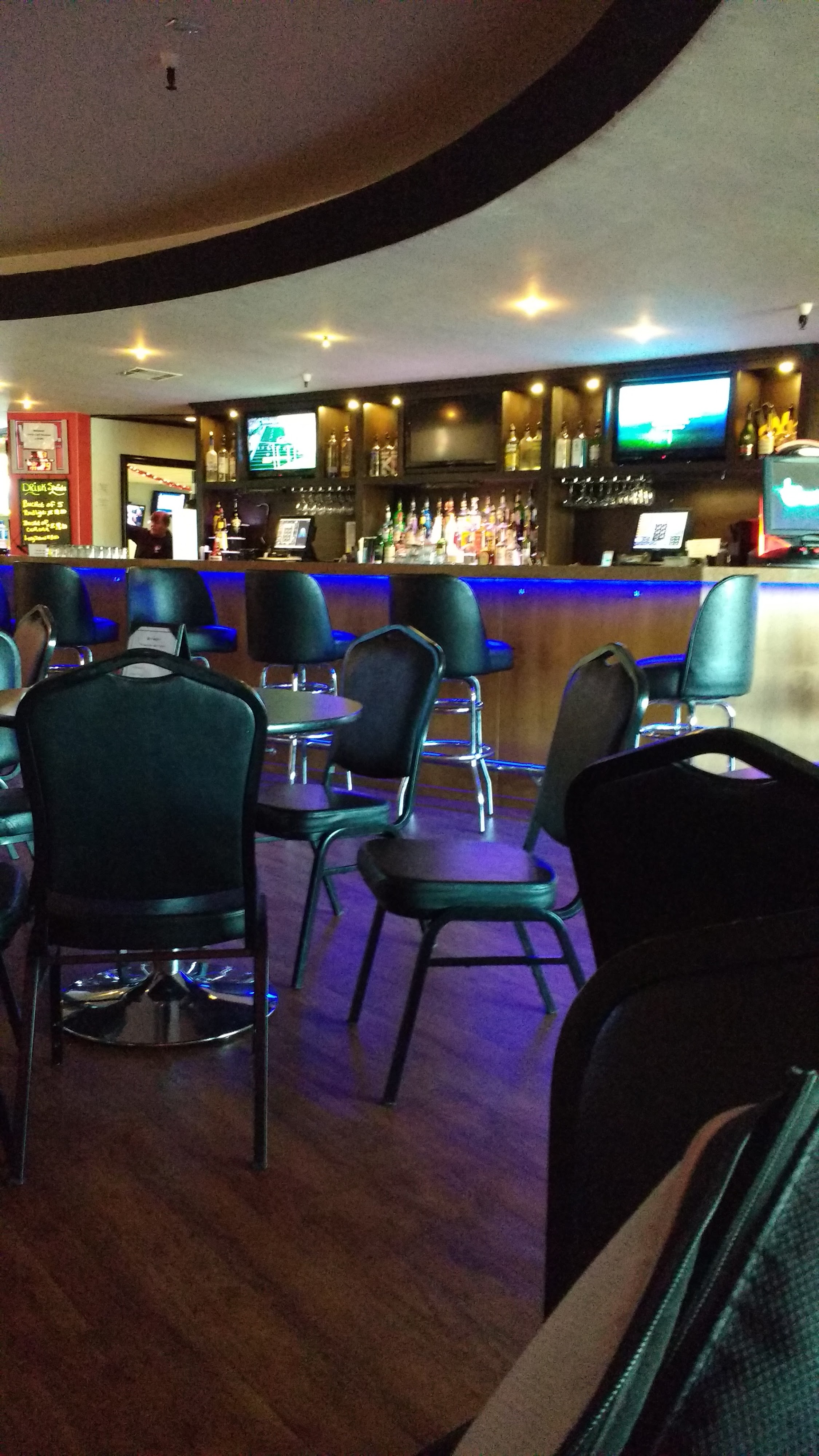 A dimly lit modern bar with blue LED lighting, black chairs, and several TVs showing sports.
