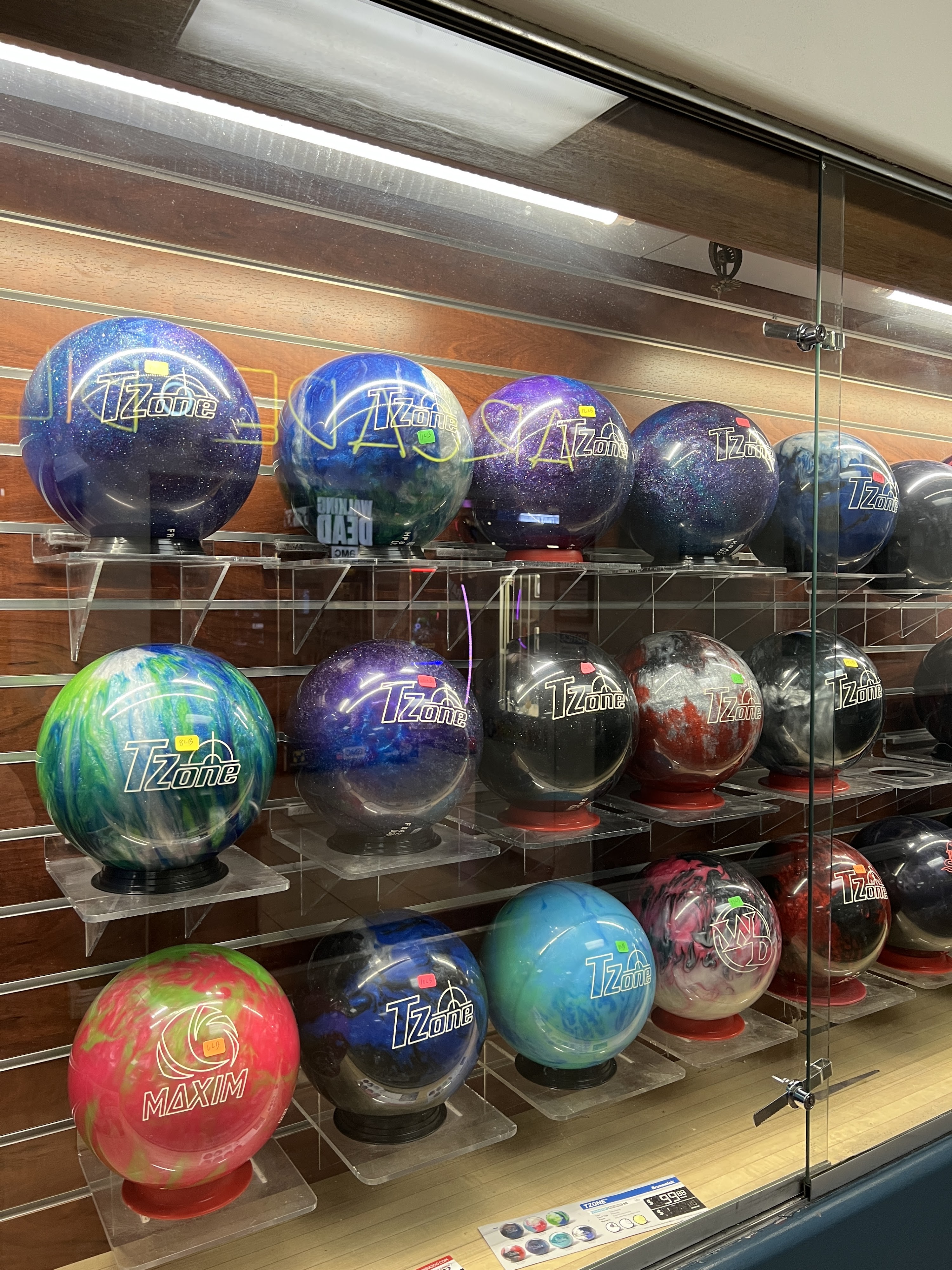 A glass display case at a bowling pro shop containing several rows of colorful bowling balls on stands.