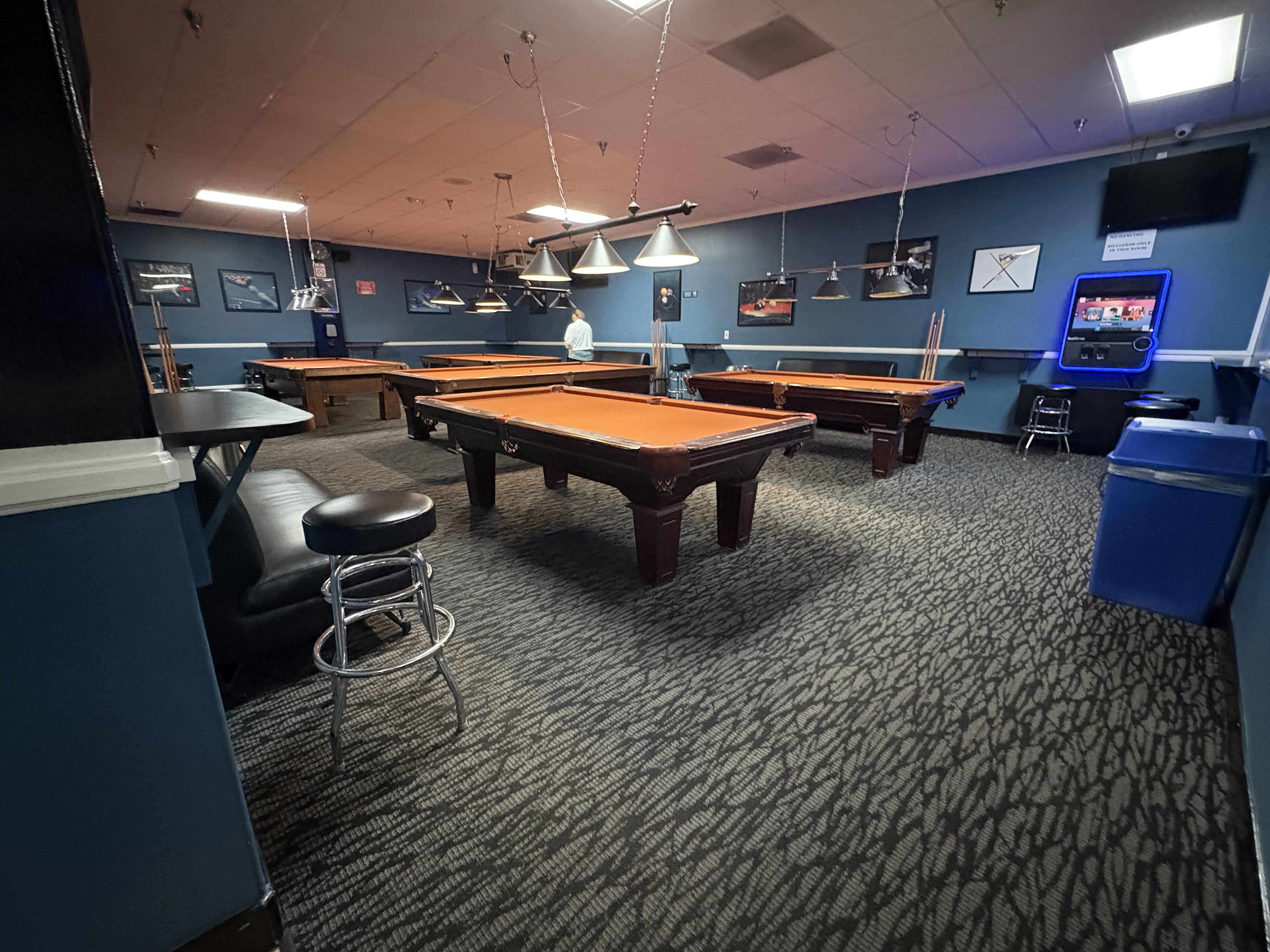 A billiards room with multiple pool tables featuring orange felt under hanging cone lights.