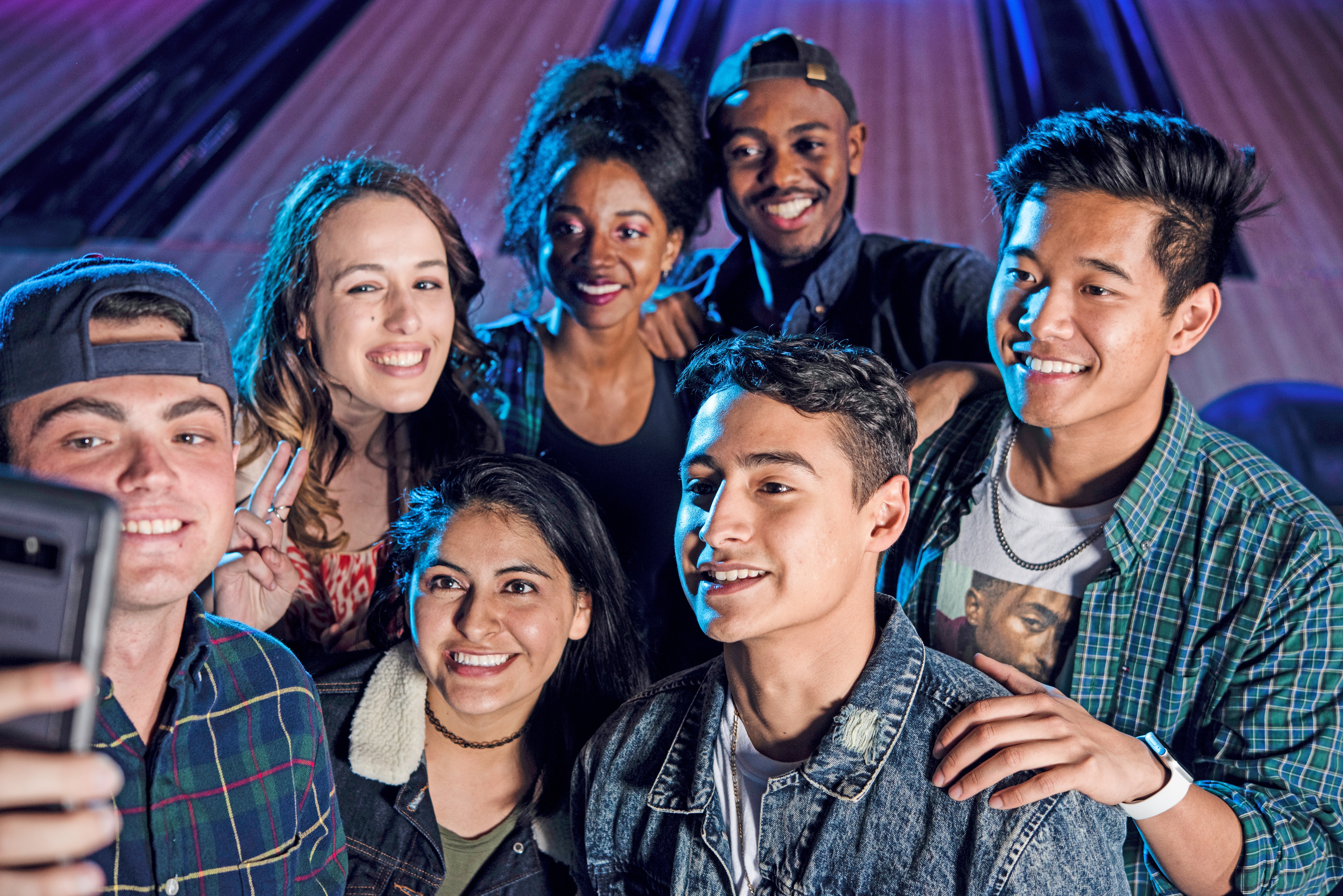 A group of diverse young friends smiling and taking a selfie in front of glowing cosmic bowling lanes.