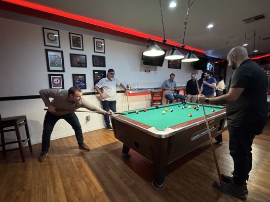 A group of men gathered around a green billiard table playing pool in a lounge.