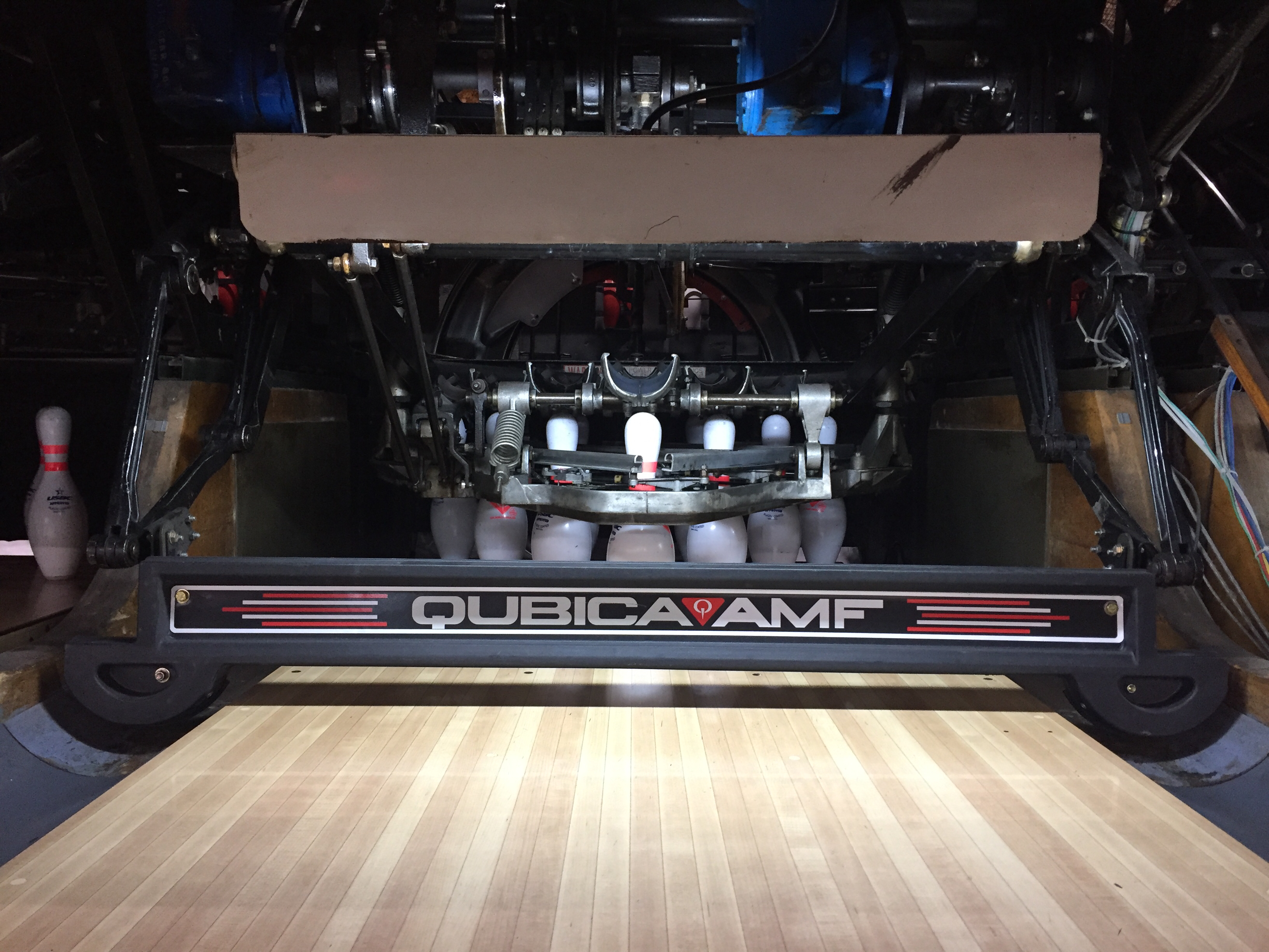 A close-up view of the QubicaAMF pinsetter machinery and sweep bar at the end of a wooden bowling lane.