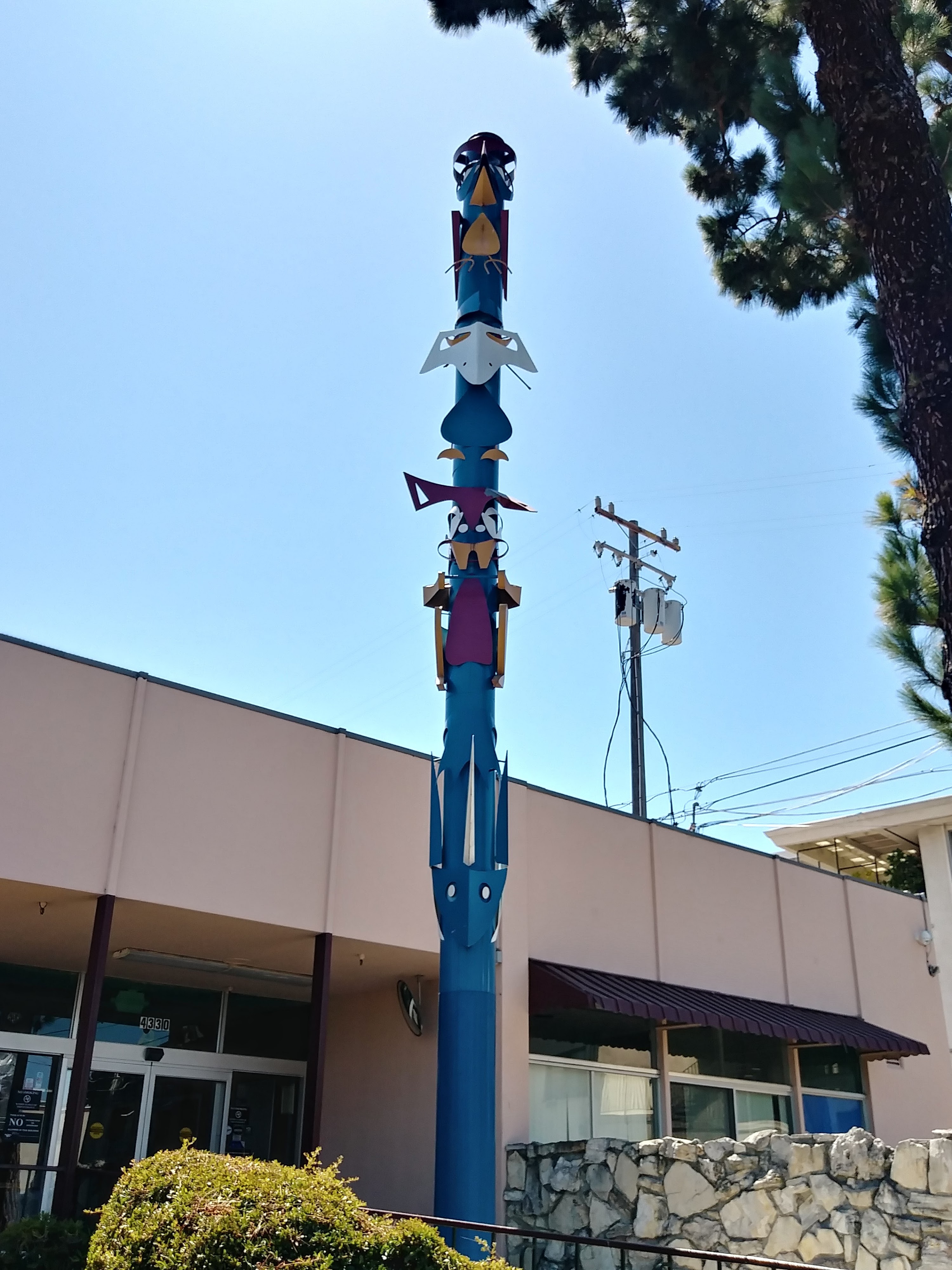 A tall blue artistic totem pole stands in front of the Bel Mateo Bowl building entrance.