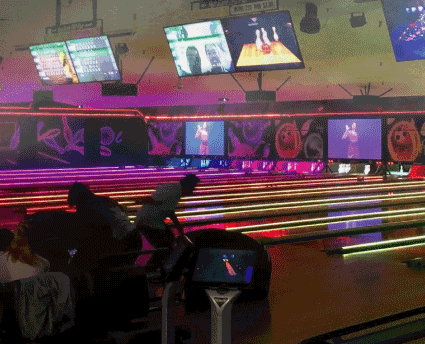 Bowlers play on lanes illuminated with neon green and pink lights during a cosmic bowling session.