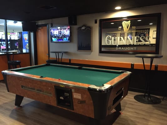 A green felt billiard table in a lounge area with a Guinness mirror and high-top tables.