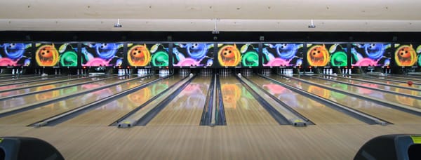 A wide-angle view of multiple polished bowling lanes with colorful graphics on the back masking units.