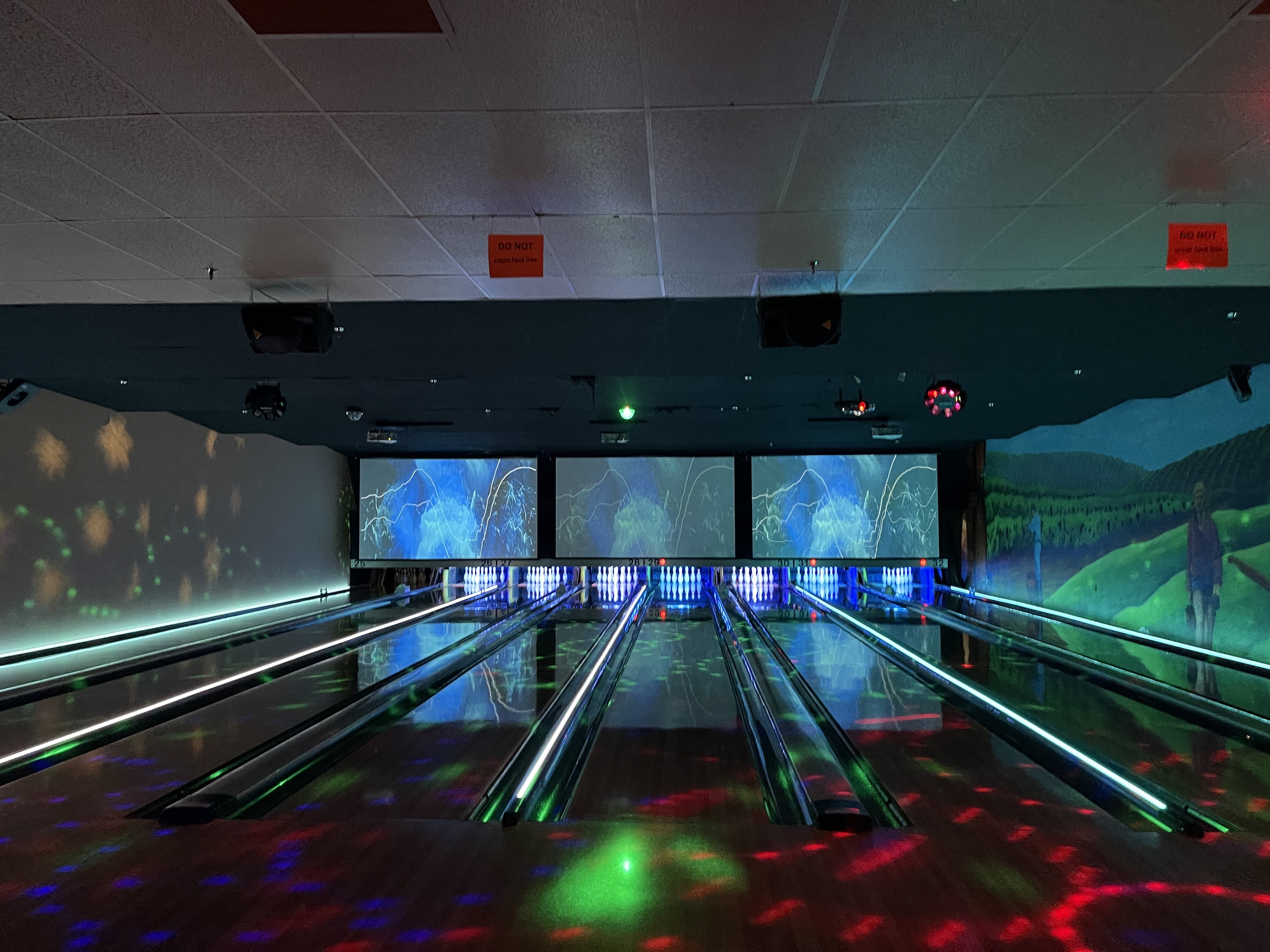Bowling lanes at night with neon green gutter lights and colorful patterns projected on the floor.