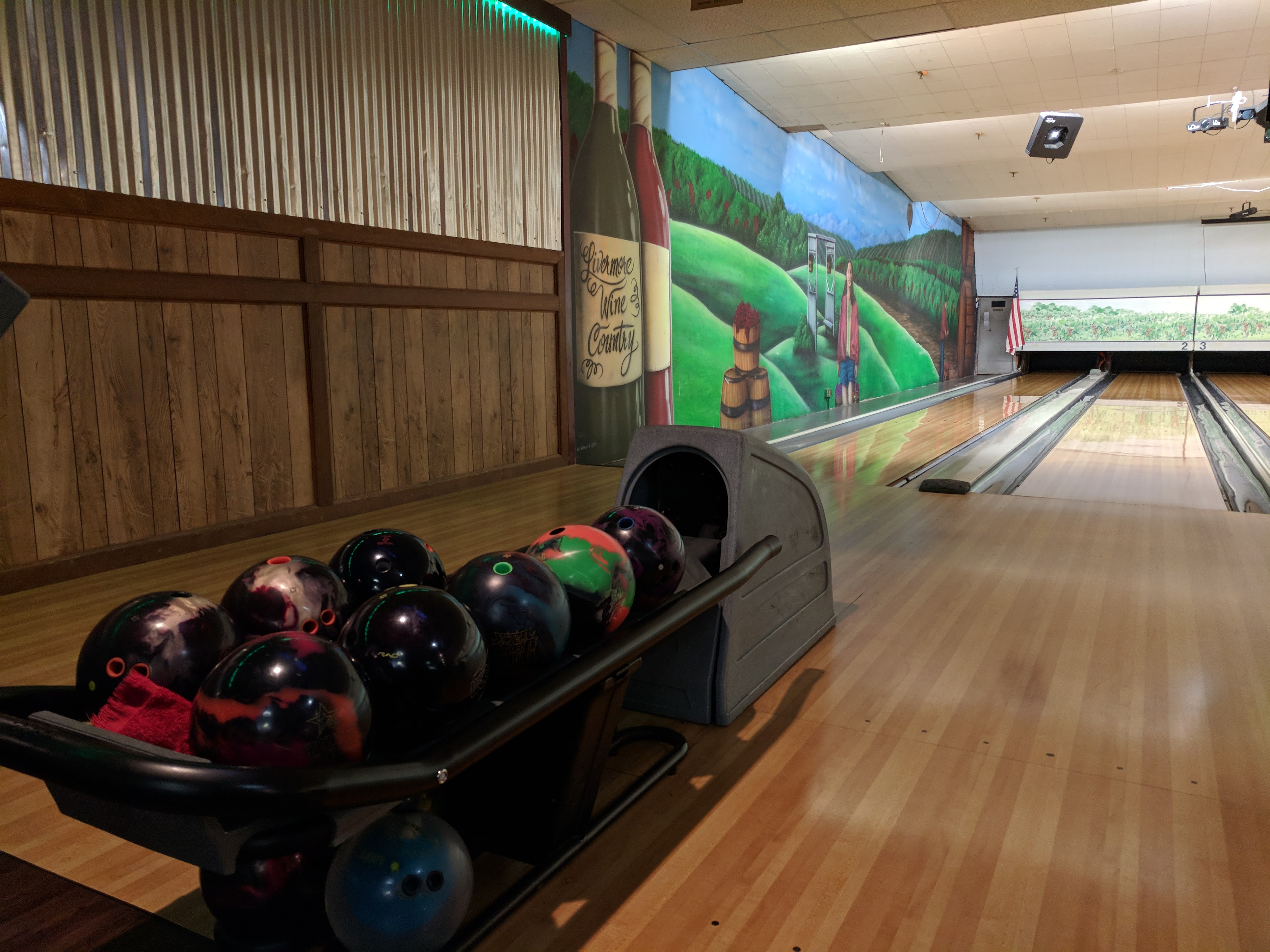 A bowling ball return rack next to a lane and a large mural depicting Livermore Wine Country.