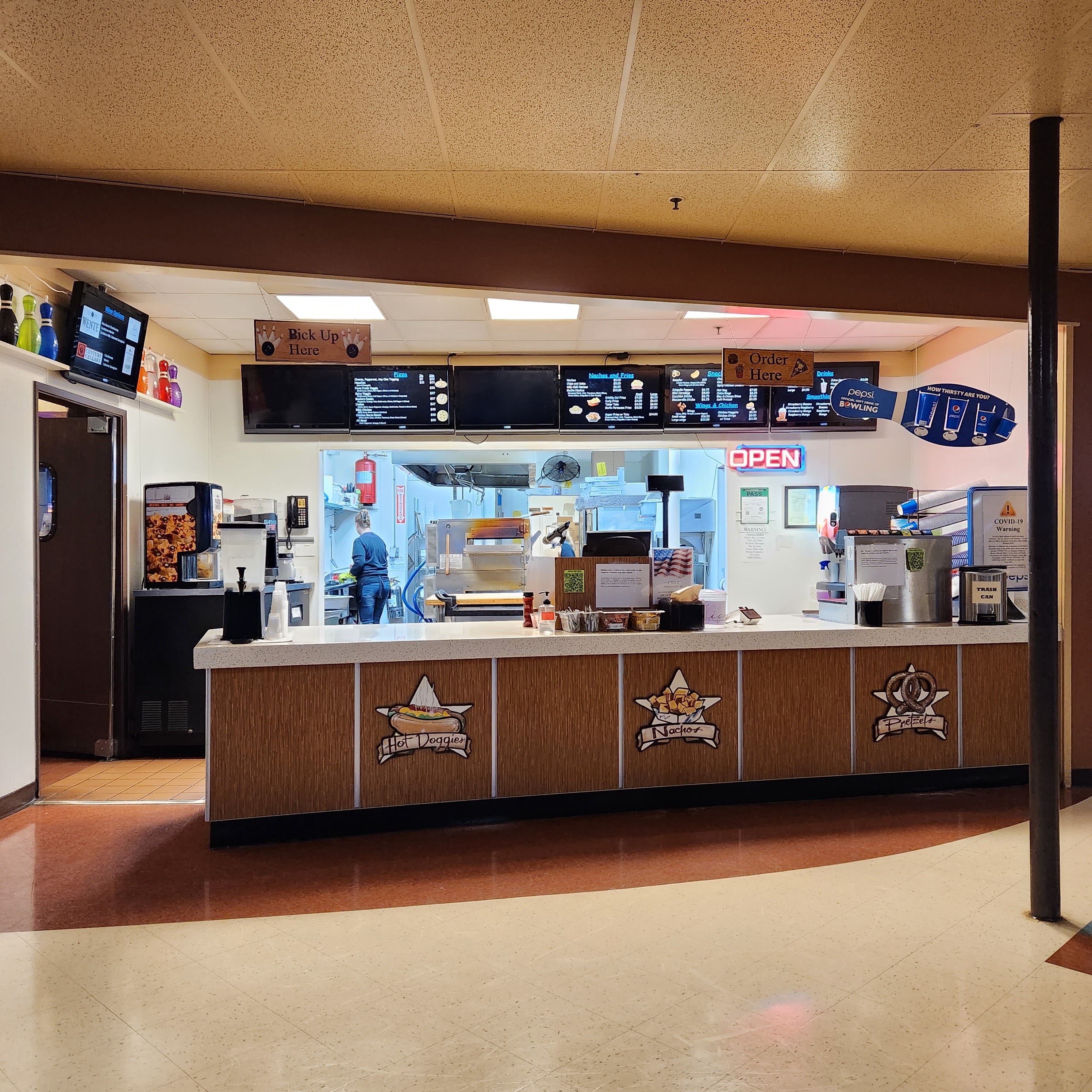 A snack bar counter with digital menu boards and graphics for hot dogs, nachos, and pretzels.