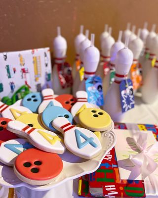 Bowling themed cookies shaped like pins and balls on a white plate for a child's birthday party.
