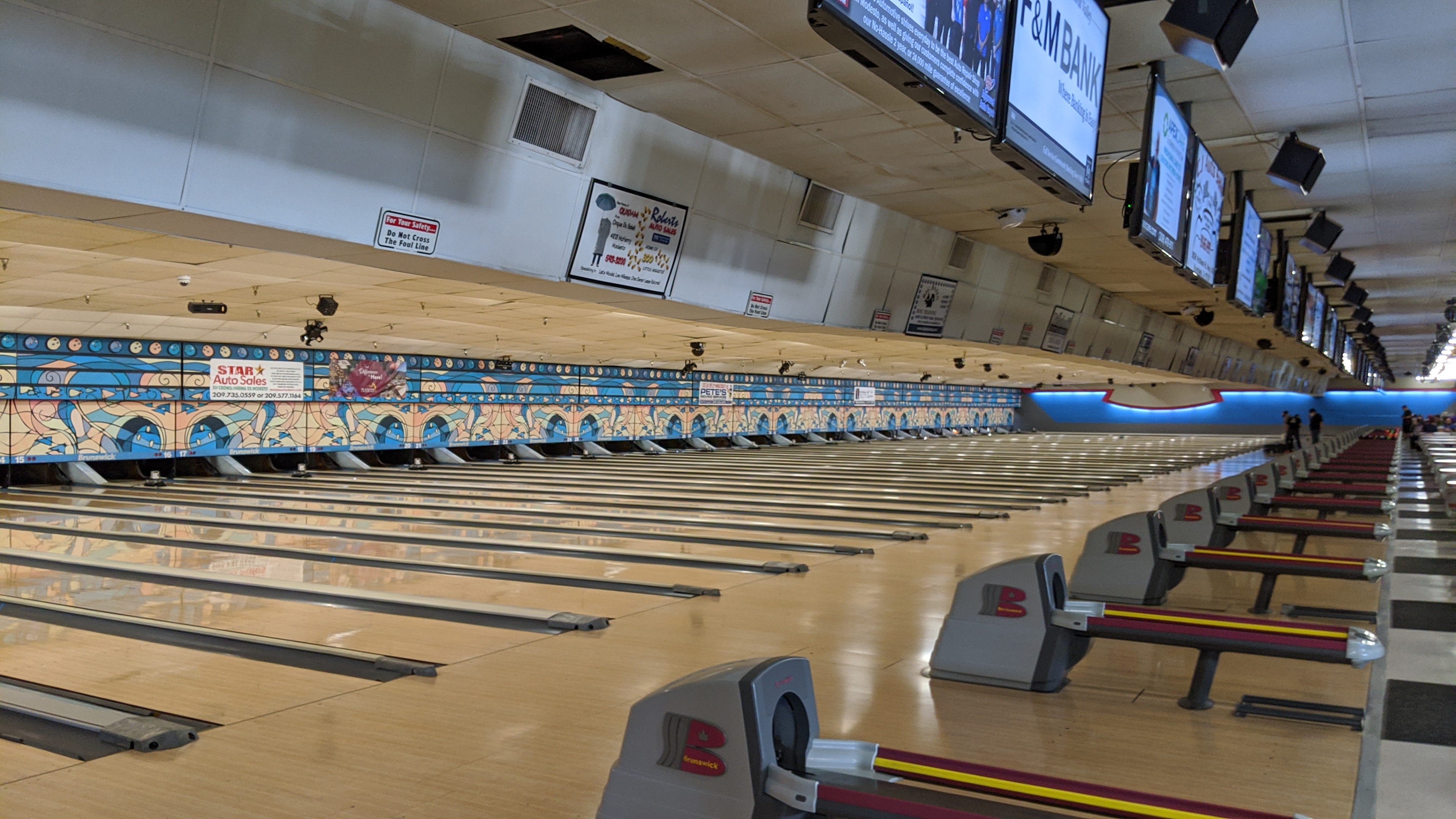 A wide view of many professional bowling lanes with ball returns and overhead monitors at McHenry Bowl.