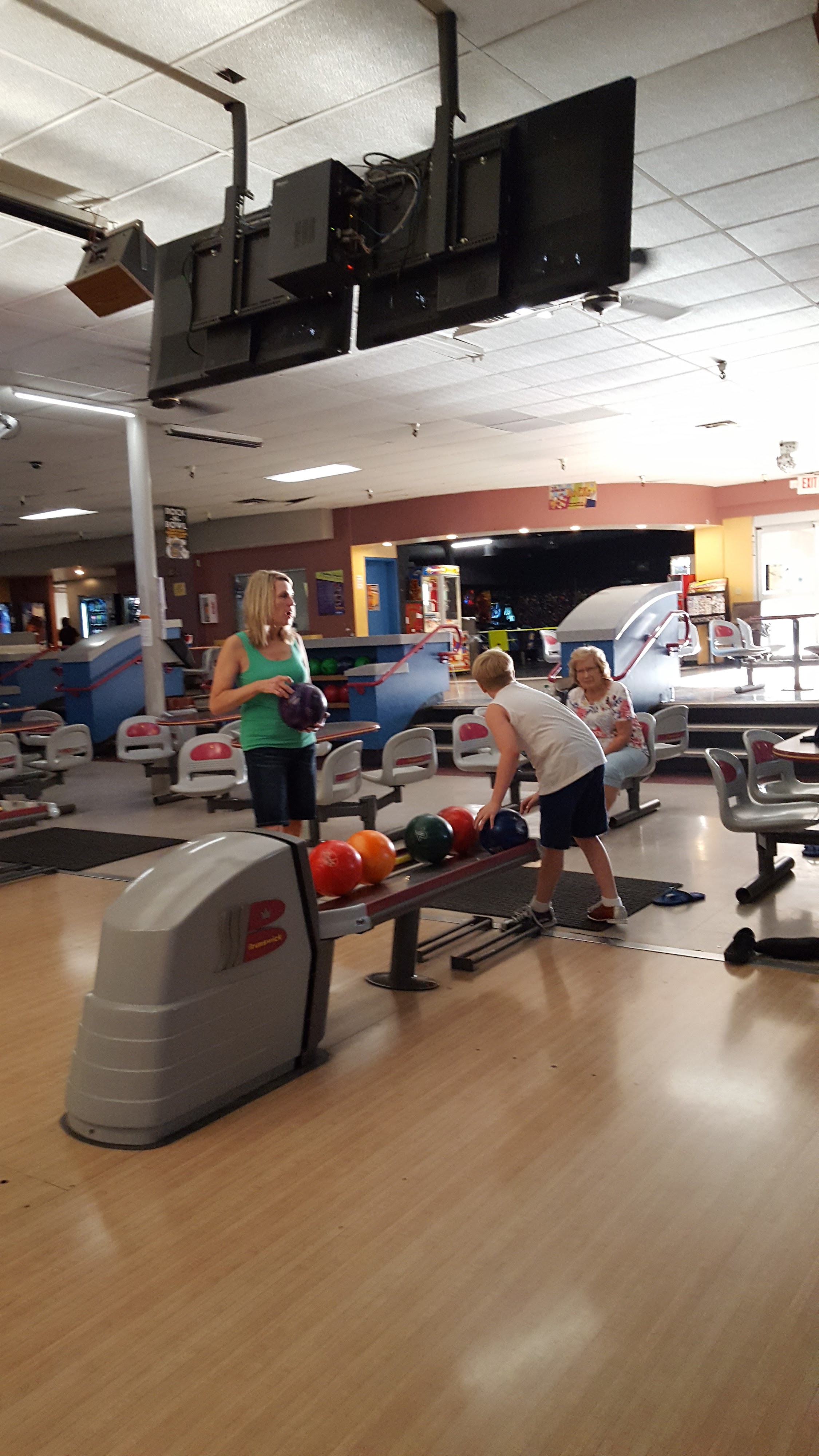 A woman and a young boy select bowling balls from a return at an indoor bowling center.