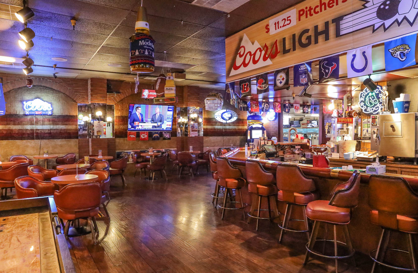The interior of a bowling center bar with leather stools, small tables, sports flags, and a television.
