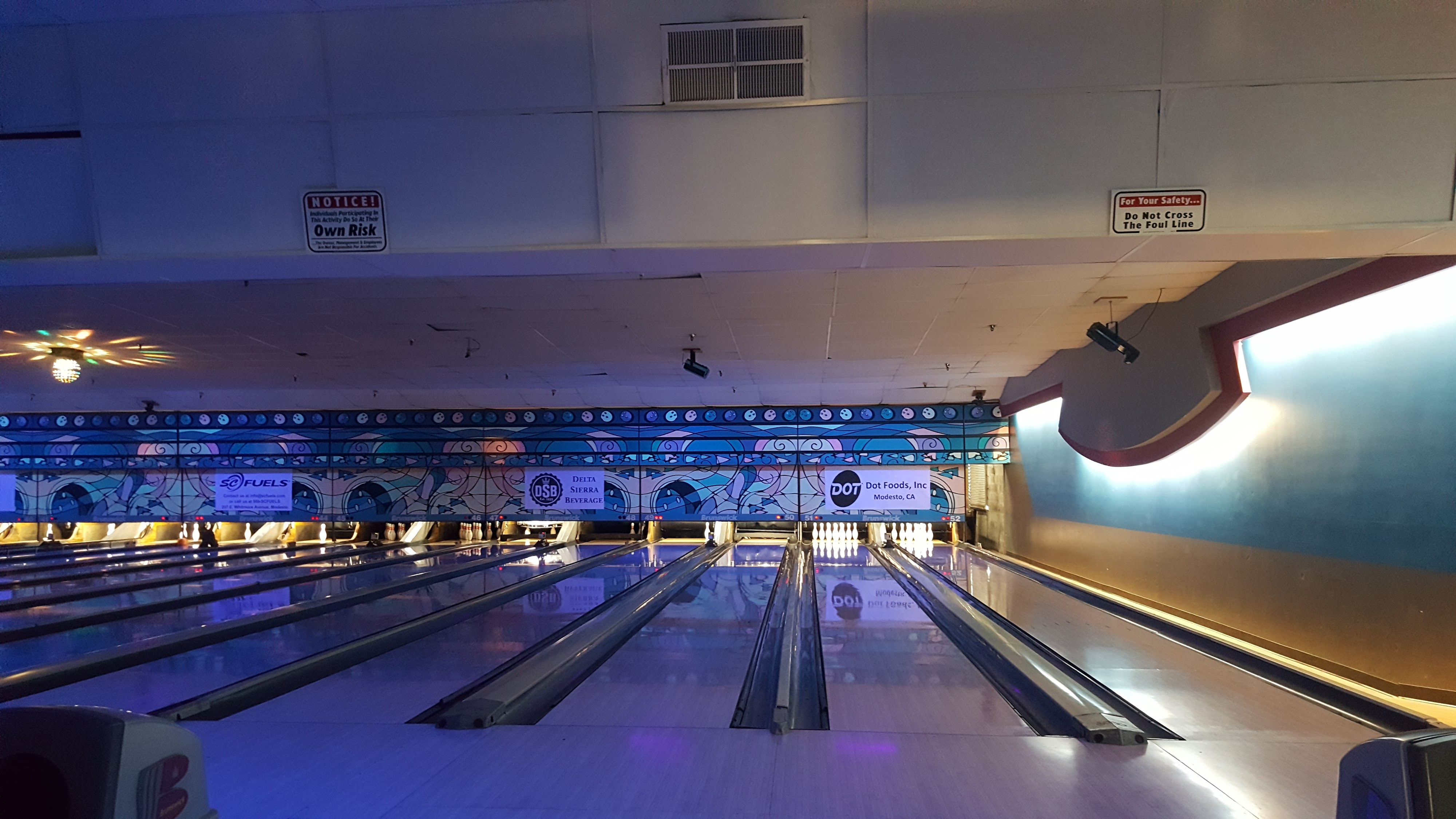 View of several polished bowling lanes at McHenry Bowl with sponsor signs and safety notices above the pins.