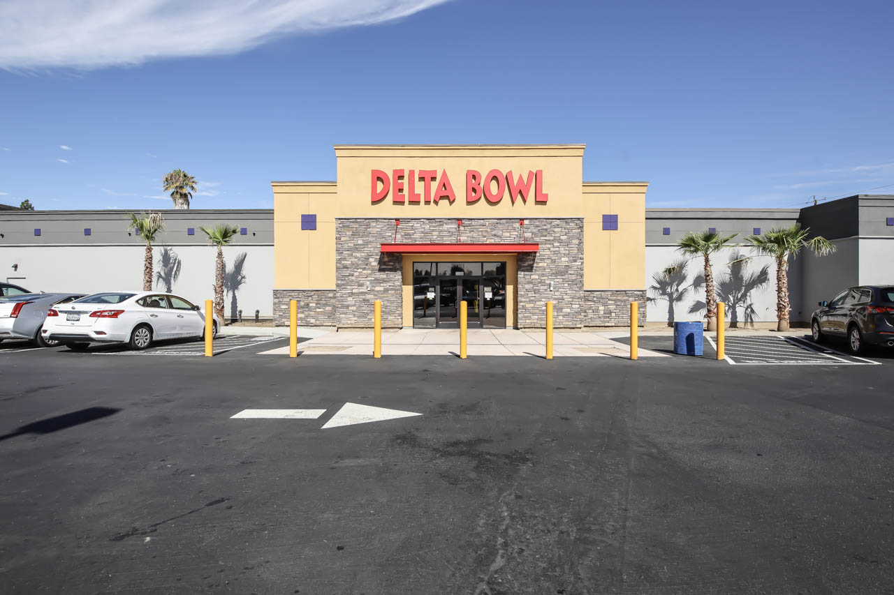 The exterior entrance of Delta Bowl featuring red signage and stone accents under a clear blue sky.