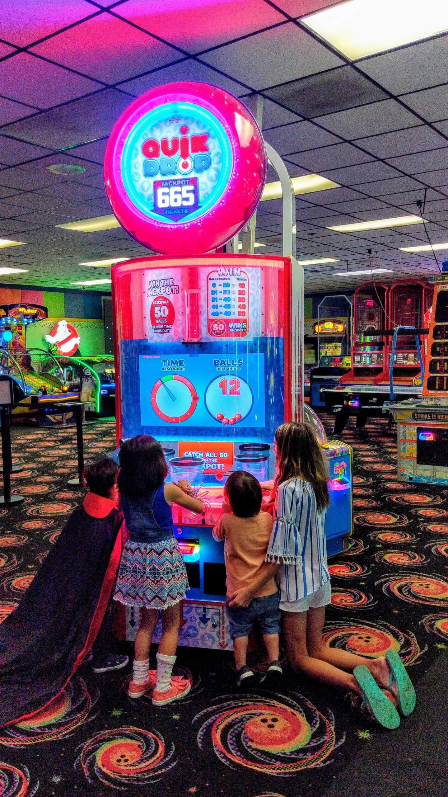 Four children play a Quik Drop arcade game in a colorful bowling center game room.